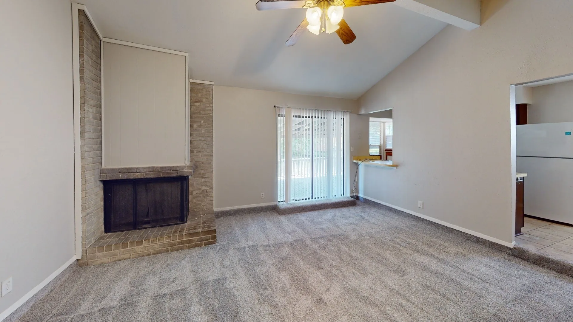 Vaulted ceiling living area with a brick fireplace, ceiling fan, and sliding glass door