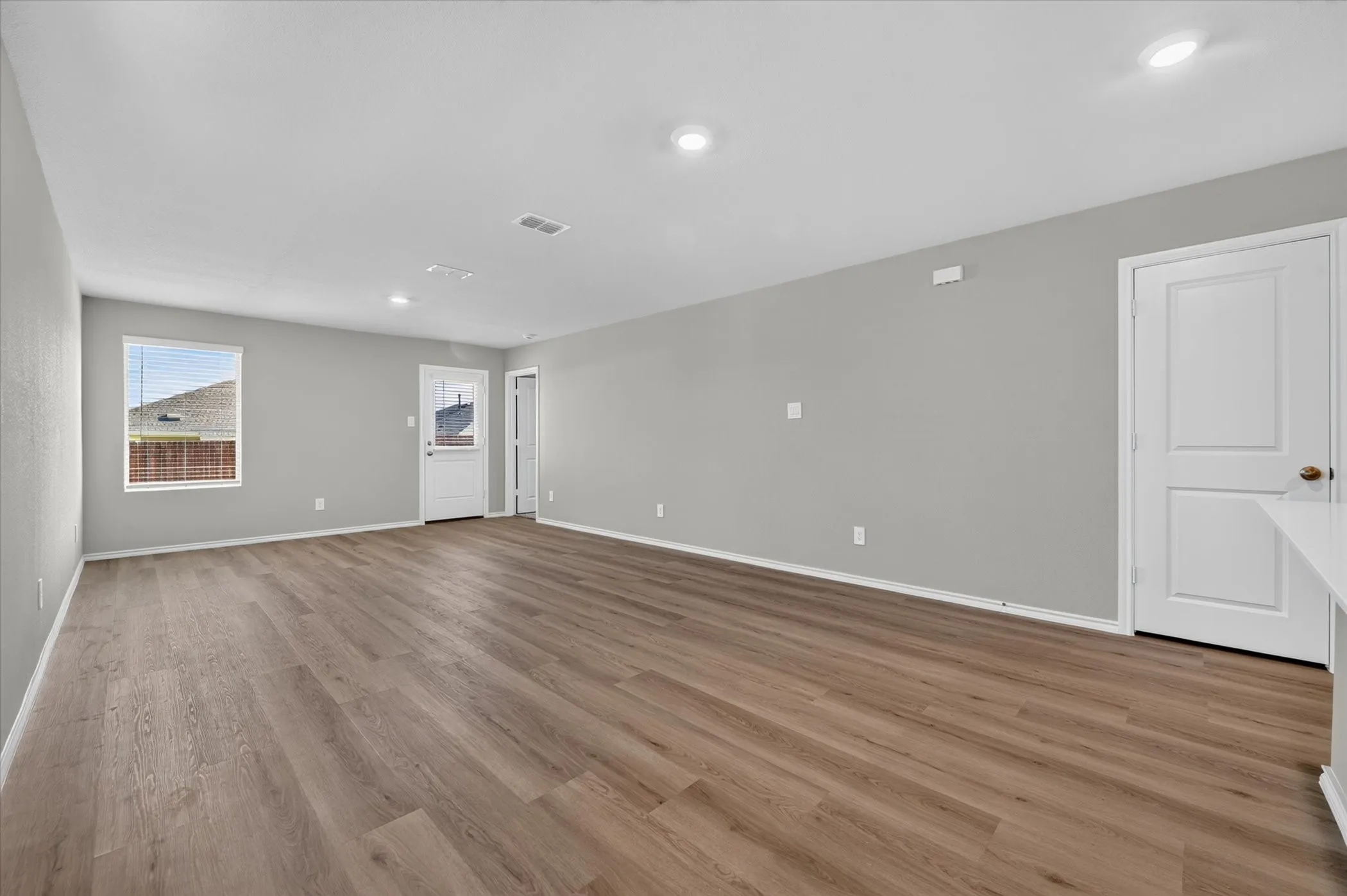 Spacious room featuring wood-finish flooring, recessed ceiling lighting, and light grey walls