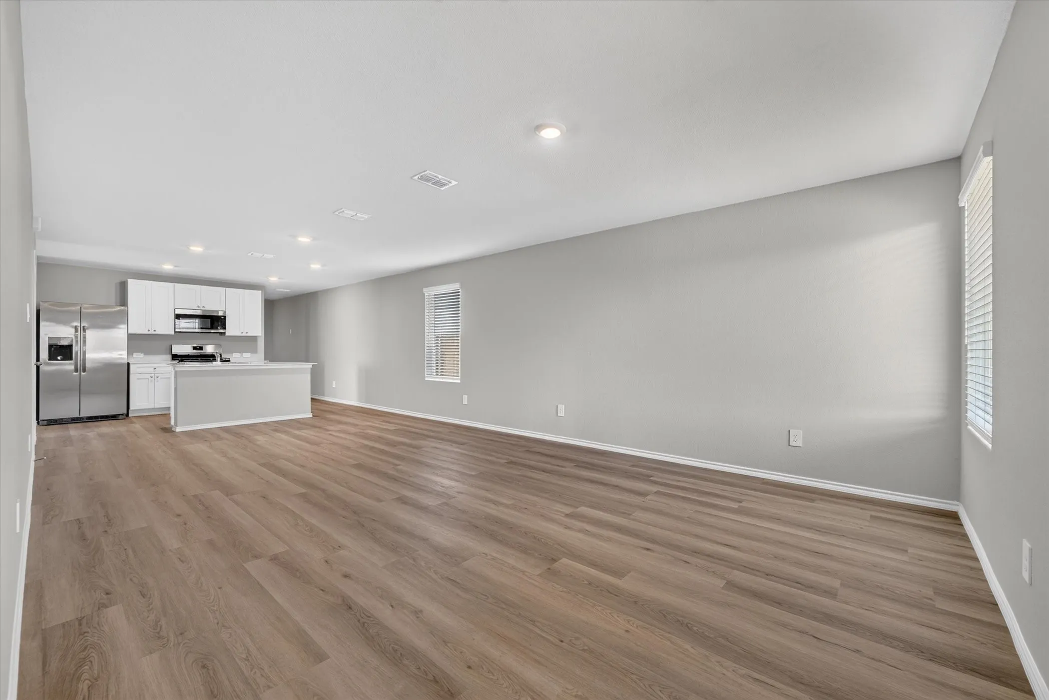 Open-concept living space featuring wood-finish flooring, recessed lighting, and a kitchen with stainless steel appliances, white cabinetry, and a central island