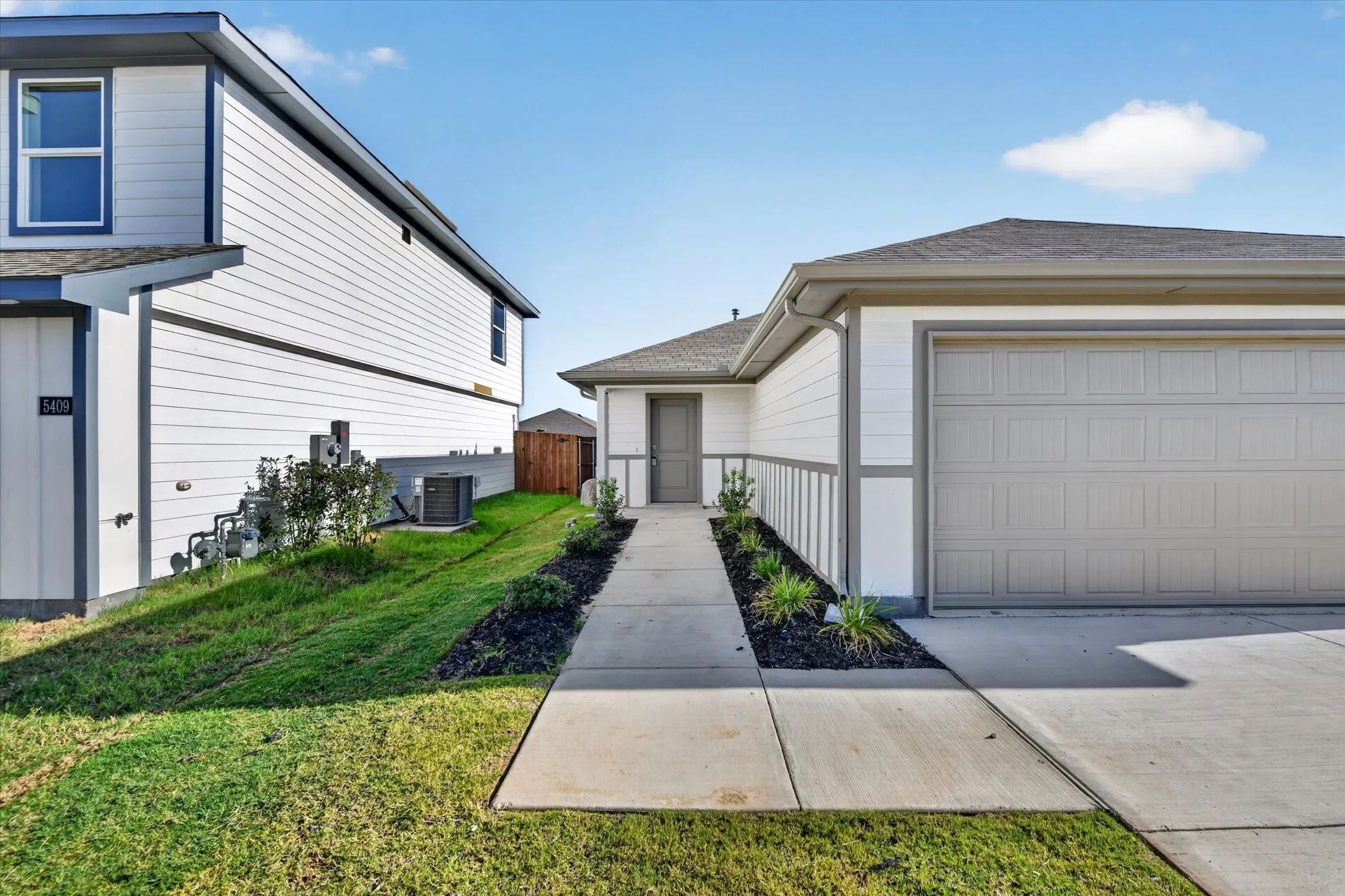 Contemporary exterior with white siding, gray trim, attached garage, concrete pathway, and landscaped planters