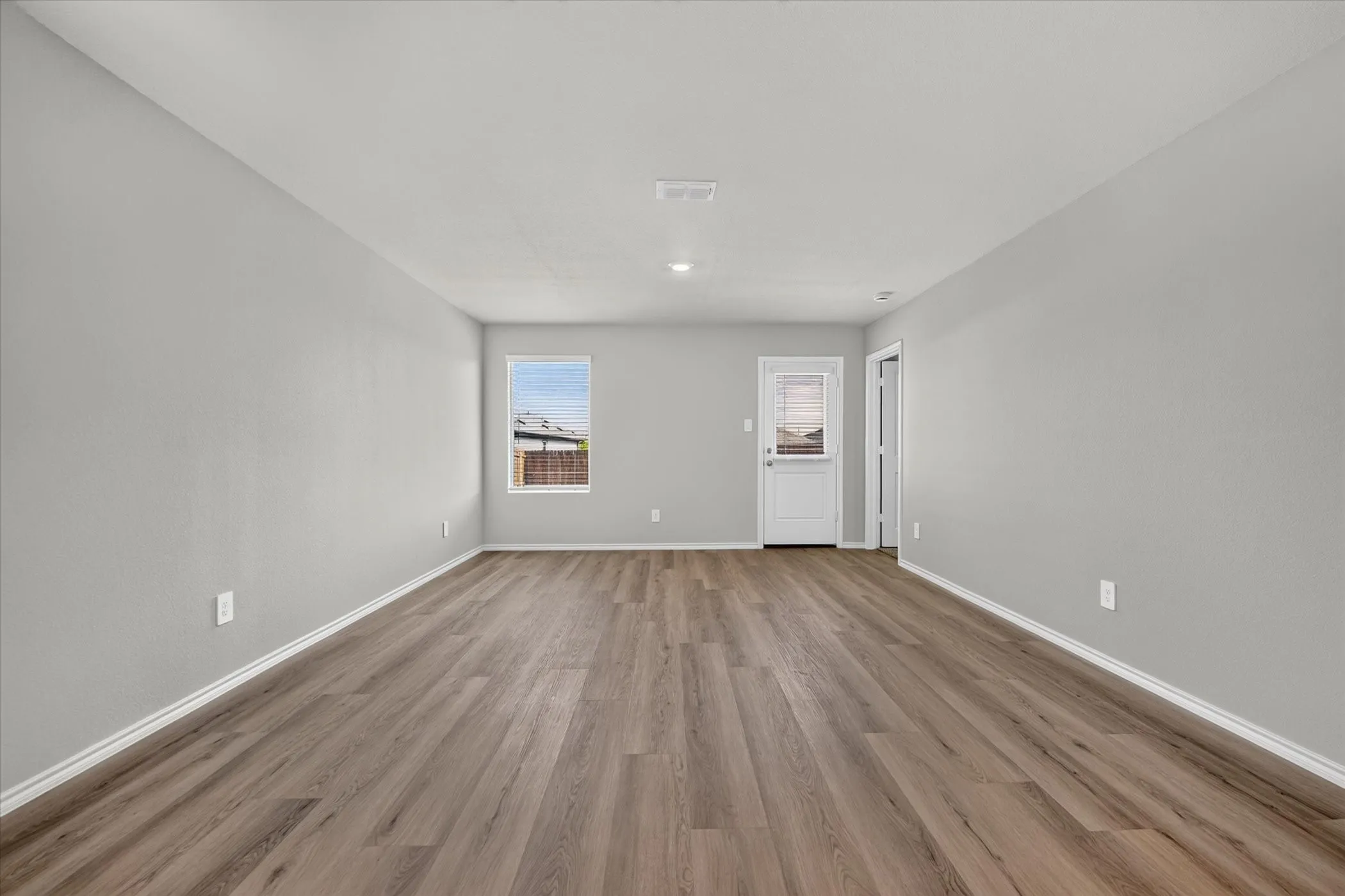 Spacious room featuring wood-finish flooring, neutral-toned walls, and a white exterior door with an inset window