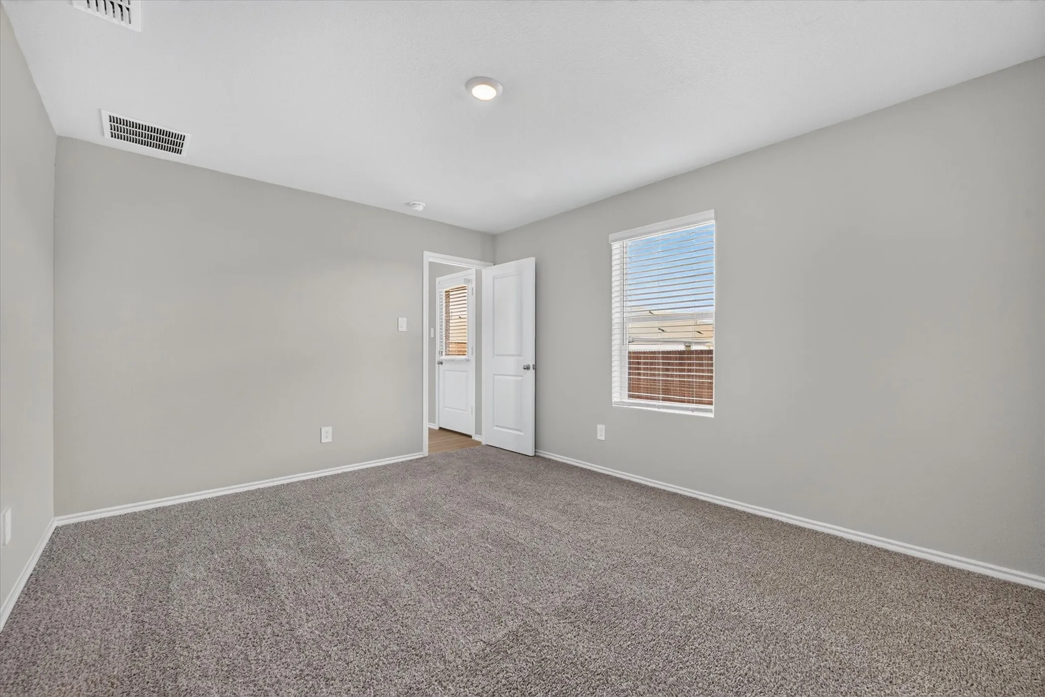 Neutral gray walls with white trim, gray carpet flooring, white window blinds, and a recessed ceiling light