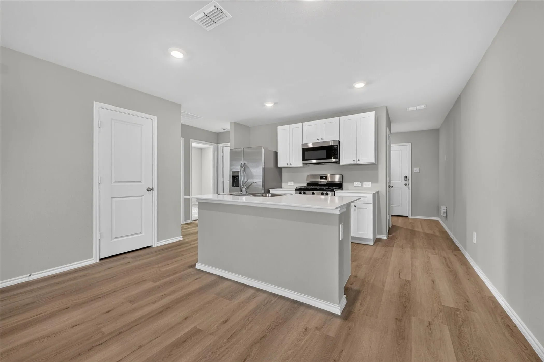 Kitchen featuring an island with white countertop, white cabinetry, stainless steel appliances, and wood-finish flooring