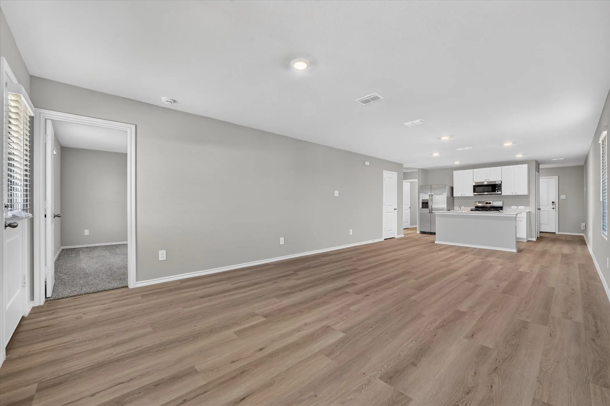 Open-concept living space featuring wood-finish flooring, recessed lighting, and a kitchen with white cabinetry, stainless steel appliances, and a central island