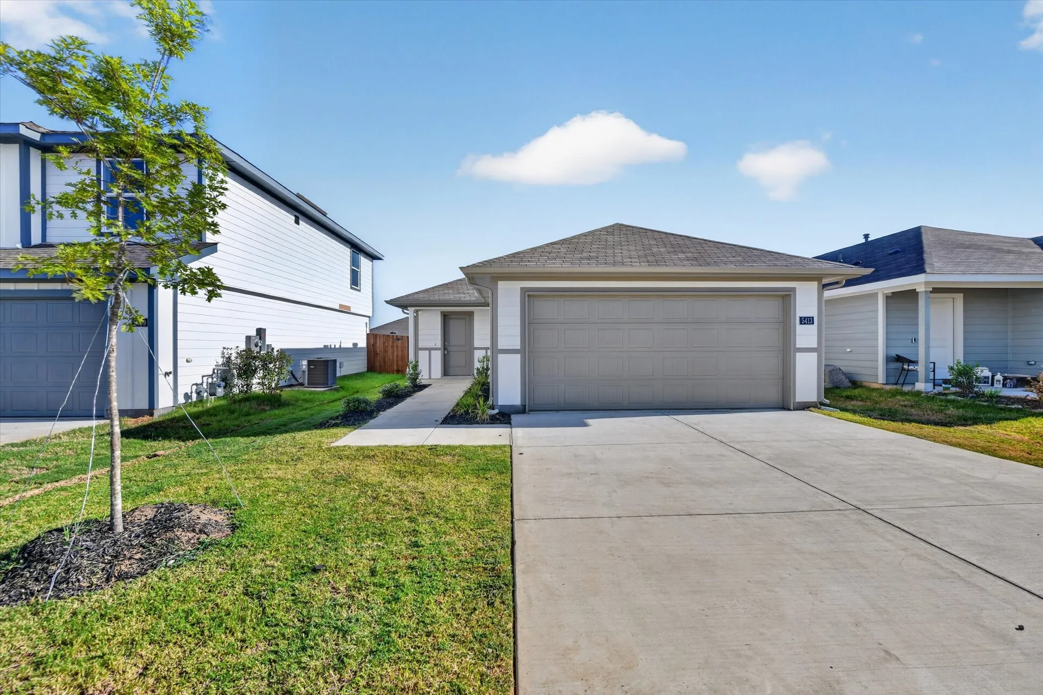 Single-story residence featuring a front-facing garage with an overhead door, a concrete driveway, a paved walkway, and a landscaped front yard