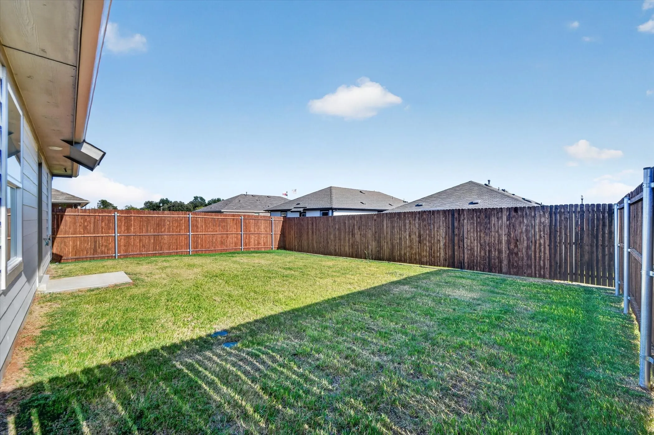 Expansive fenced backyard with a manicured lawn, complete with a concrete pad and exterior wall lighting