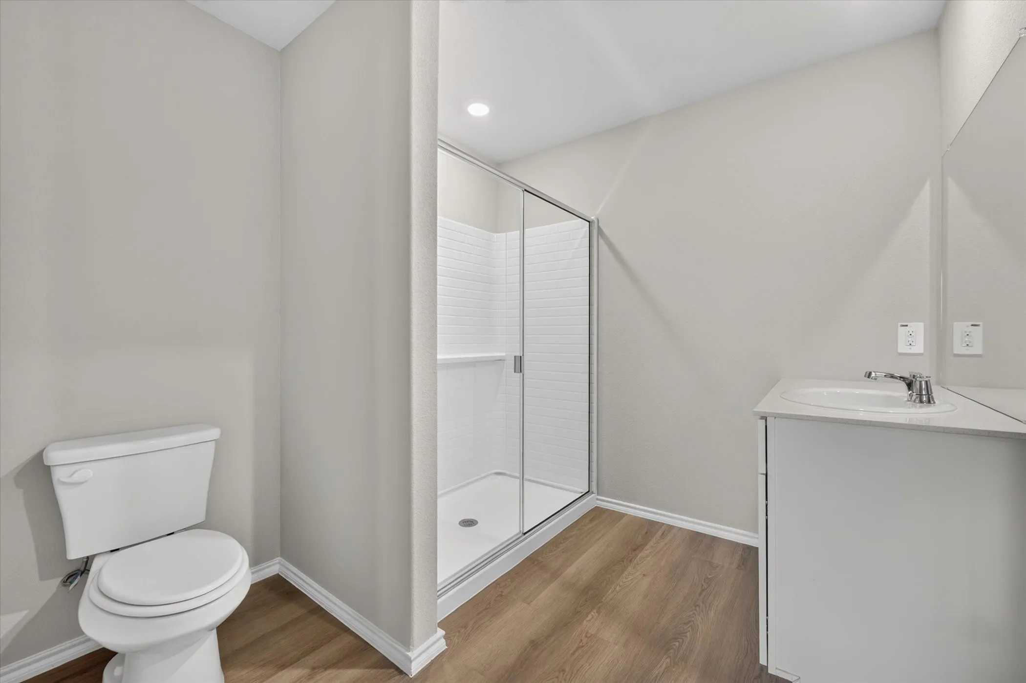 Full bathroom featuring wood-finish flooring, a glass-enclosed shower with subway tile, a white vanity with an integrated sink, and a chrome faucet
