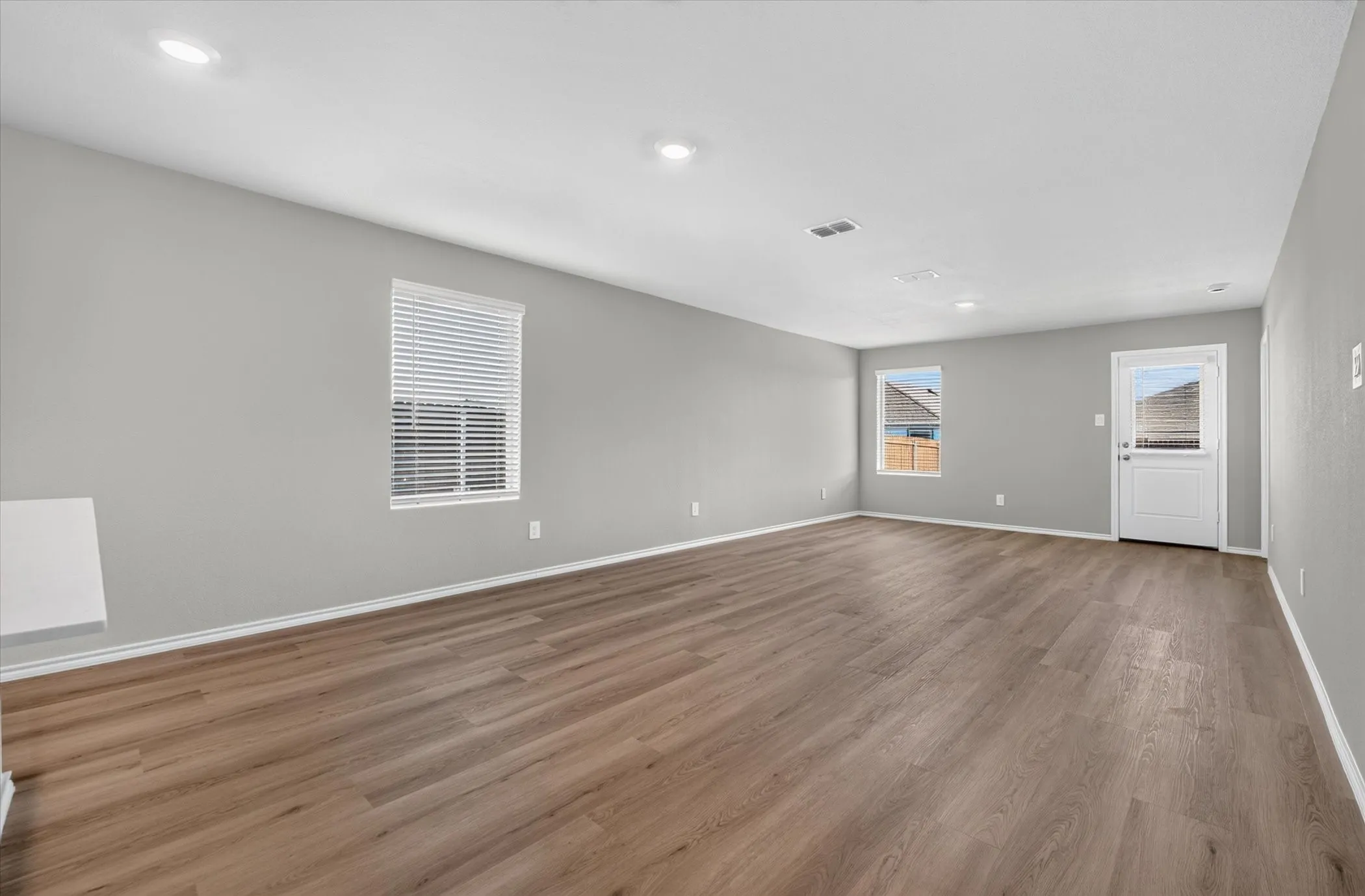 Spacious room featuring wood-finish flooring, recessed lighting, and multiple windows with blinds