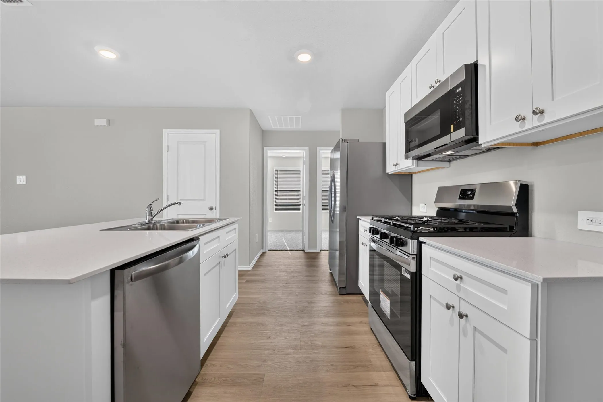Kitchen featuring an island with a double basin sink, white cabinetry, stainless steel appliances, wood-finish flooring, and recessed lighting