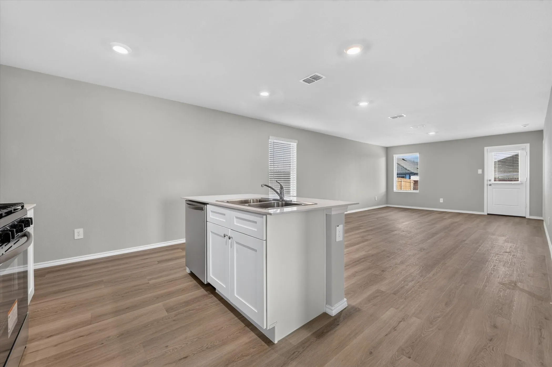 Open-concept living area featuring wood-finish flooring, recessed lighting, and a kitchen island with a double basin sink