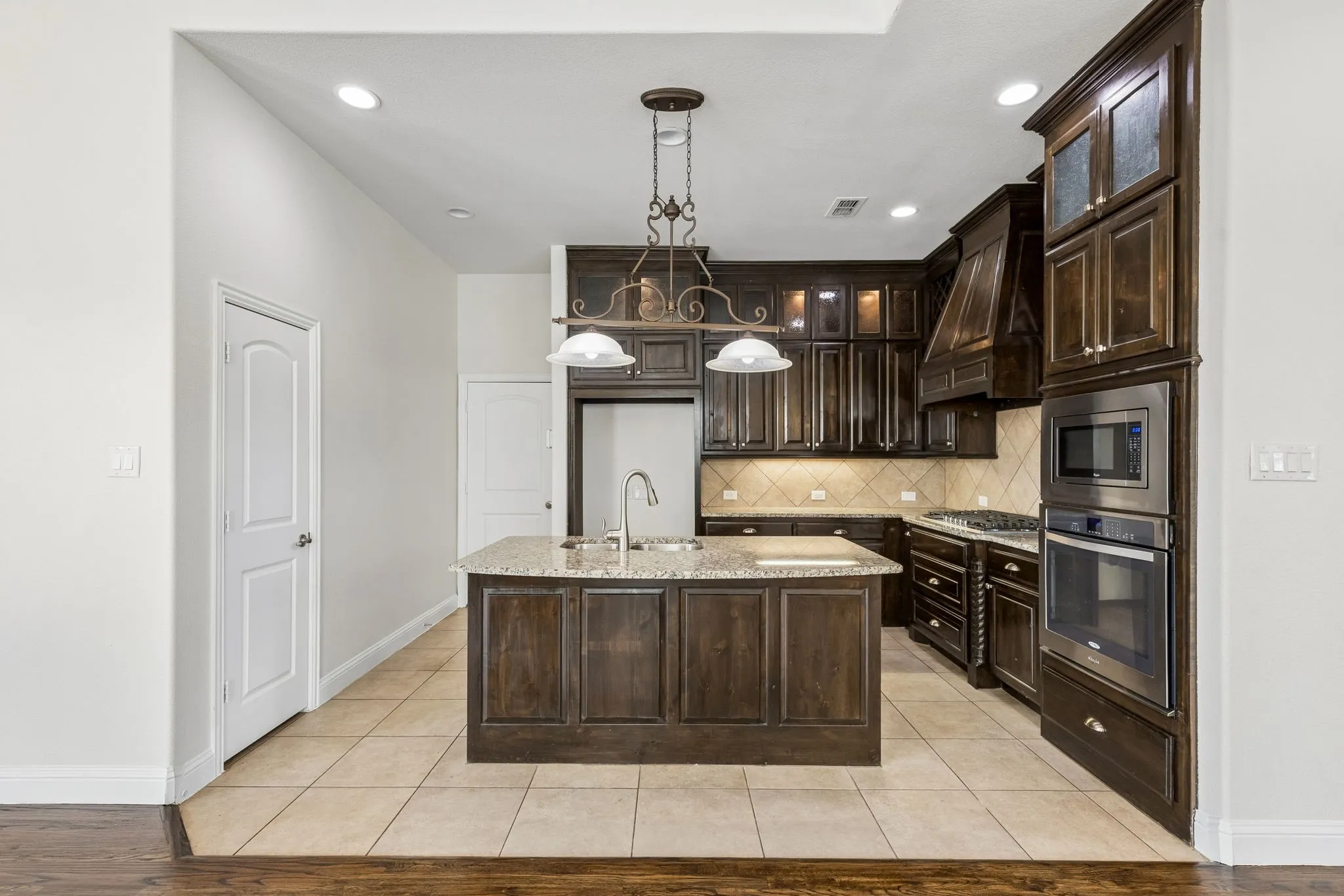 Kitchen featuring dark wood cabinetry, a central island with a granite-style countertop, stainless steel built-in appliances, and tile flooring