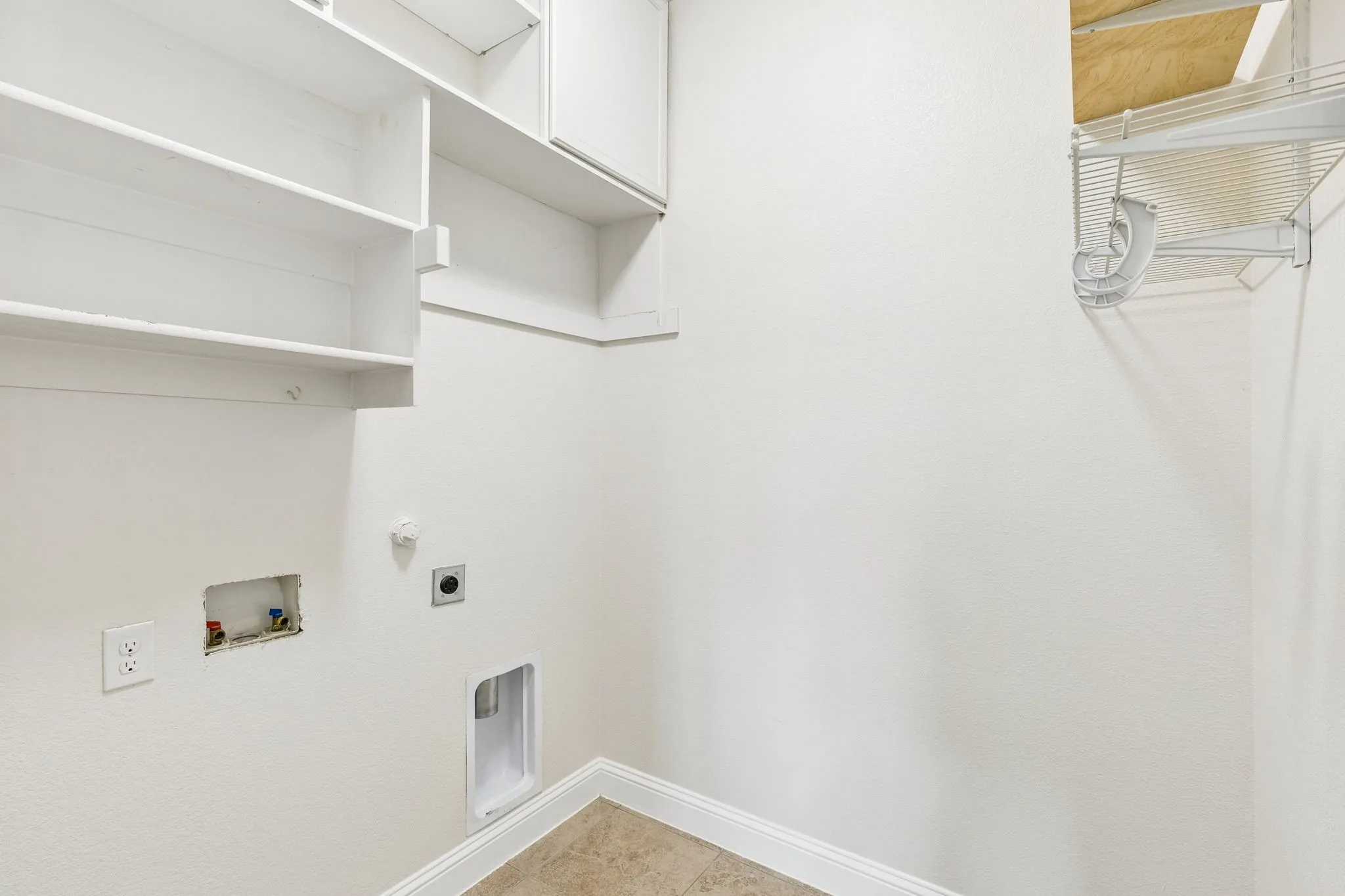 White cabinetry with built-in shelving, tile flooring, and utility hookups