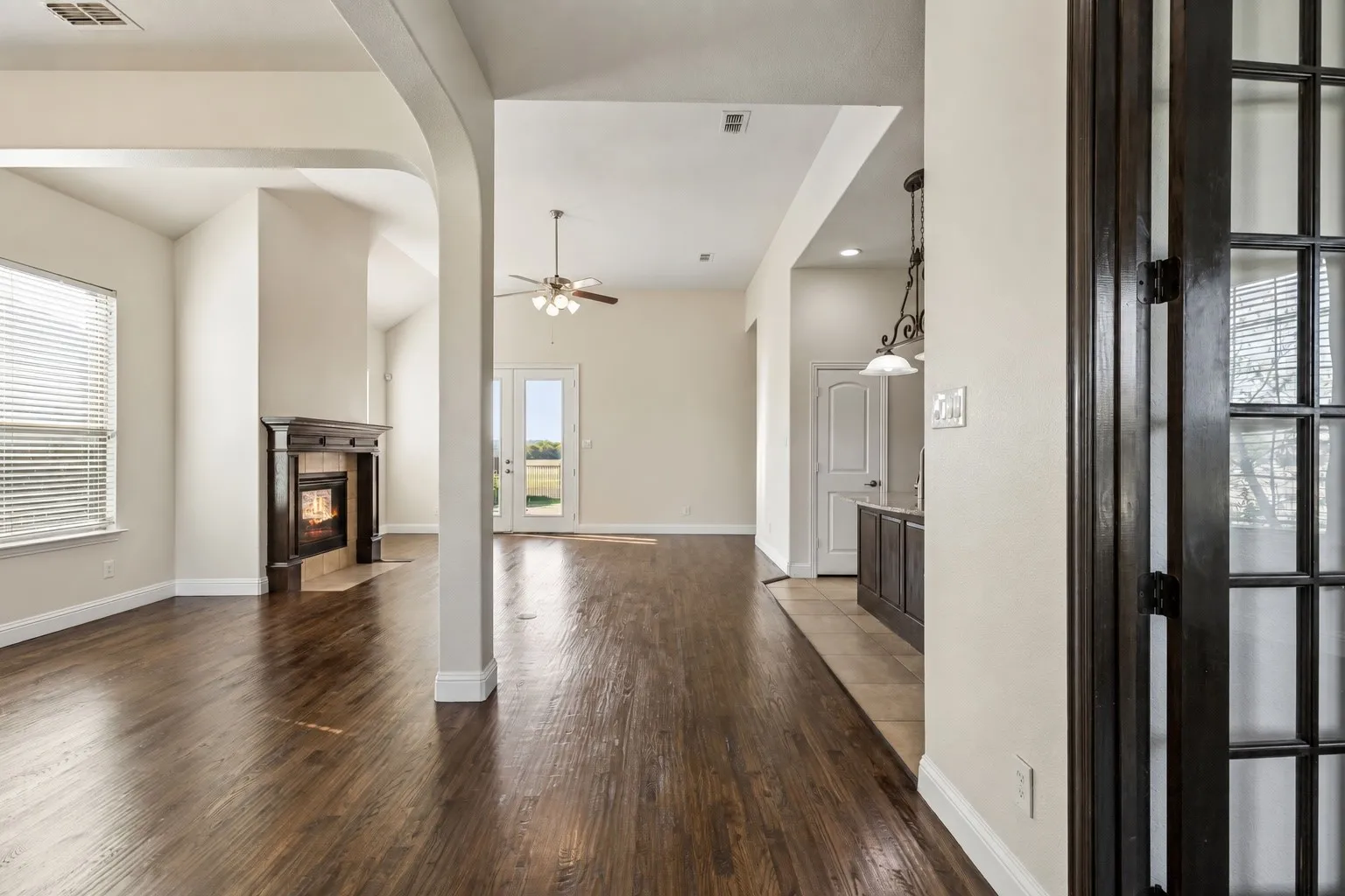 Rich wood-finish flooring throughout, a dark wood-mantled fireplace, and an arched entryway