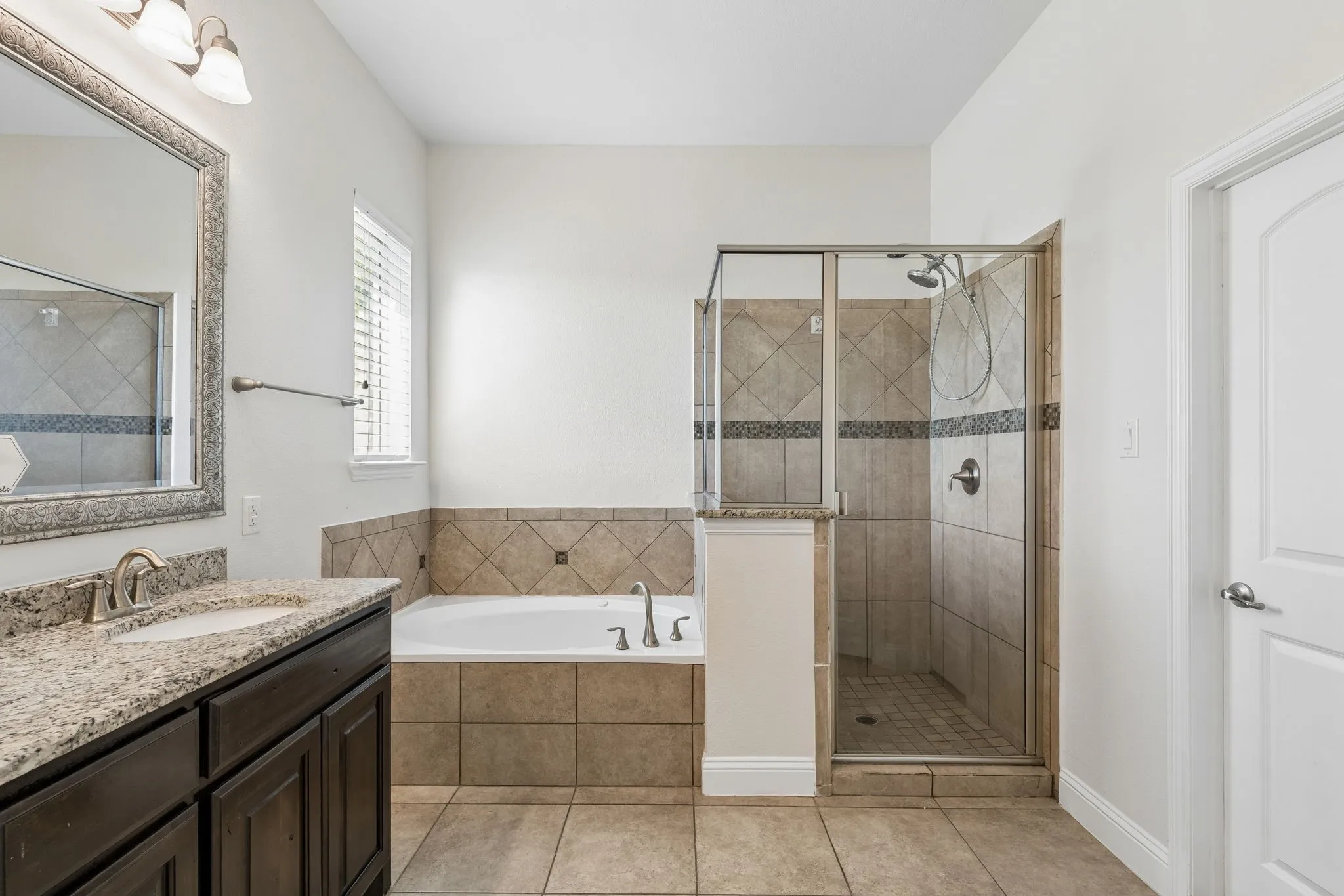 Built-in soaking tub, walk-in shower with glass enclosure, granite vanity countertop, single basin sink, and tile flooring