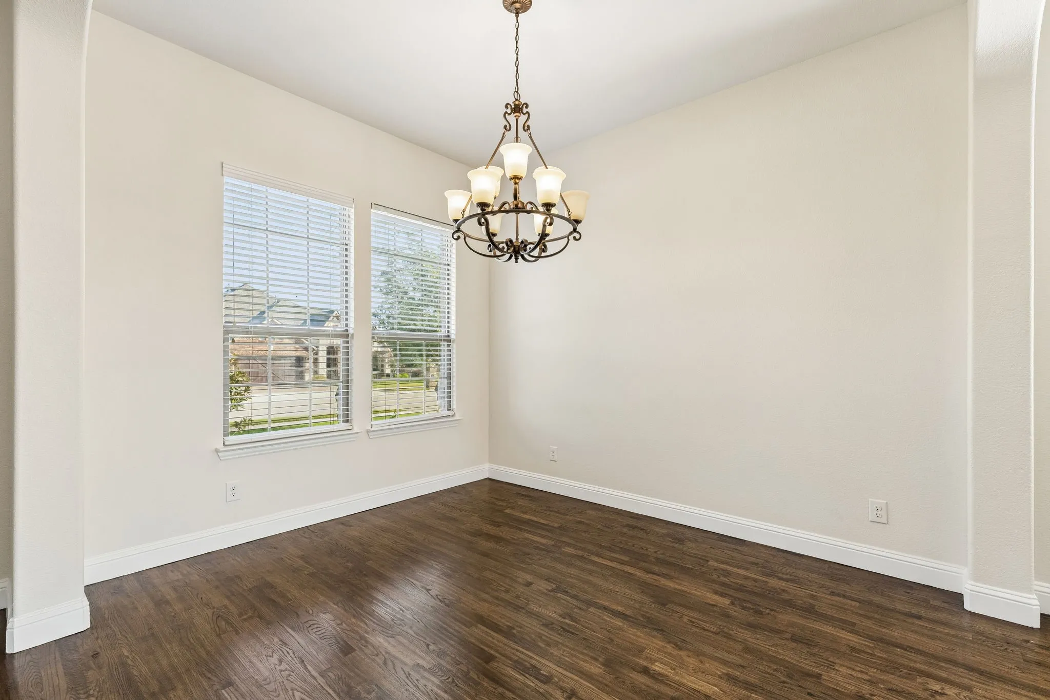 Wood-finish flooring, dual windows with blinds, recessed chandelier, and arched entryway