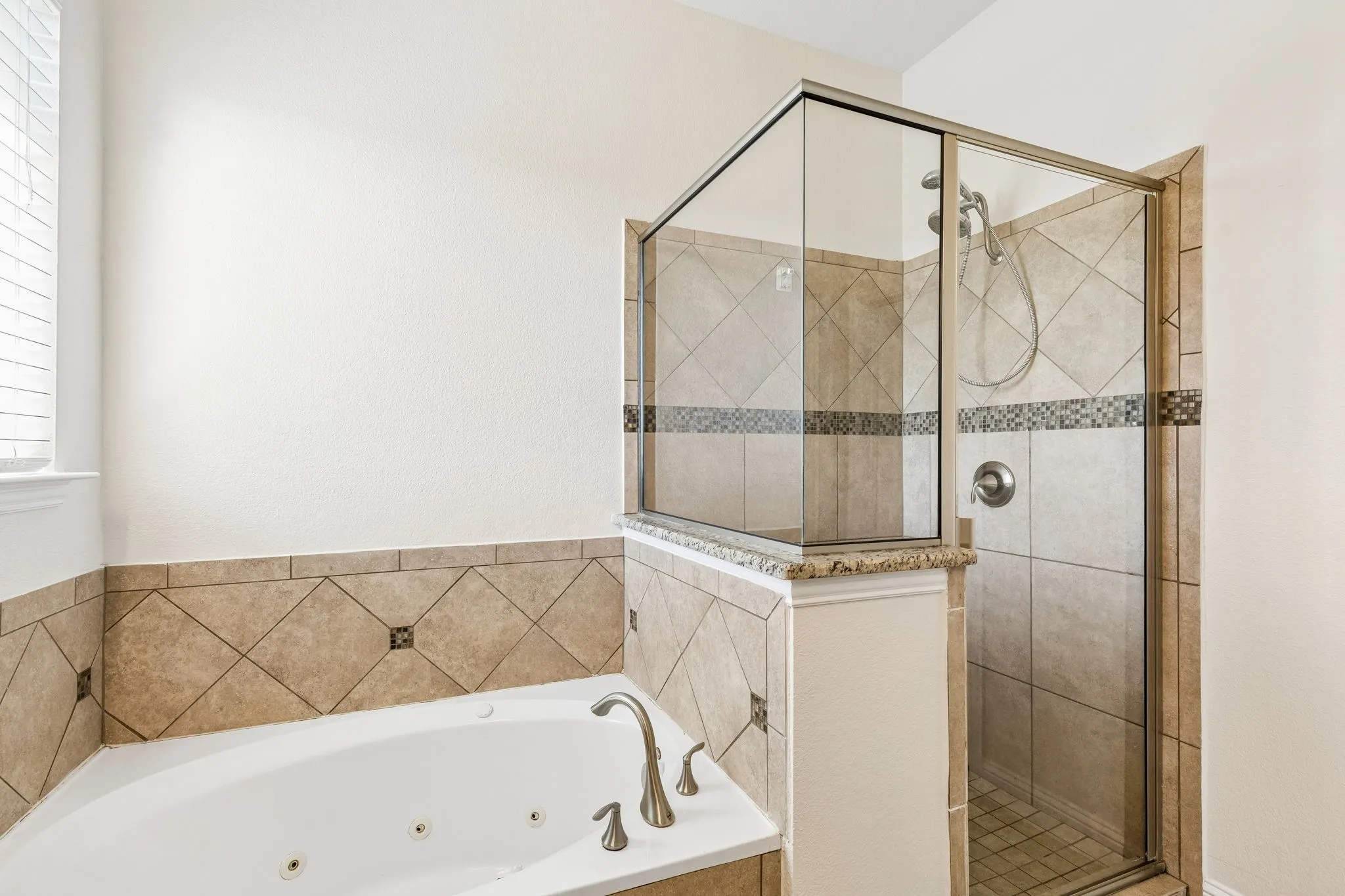 Corner soaking tub with tile surround, glass-enclosed shower, tile shower walls with decorative accent band, and chrome fixtures