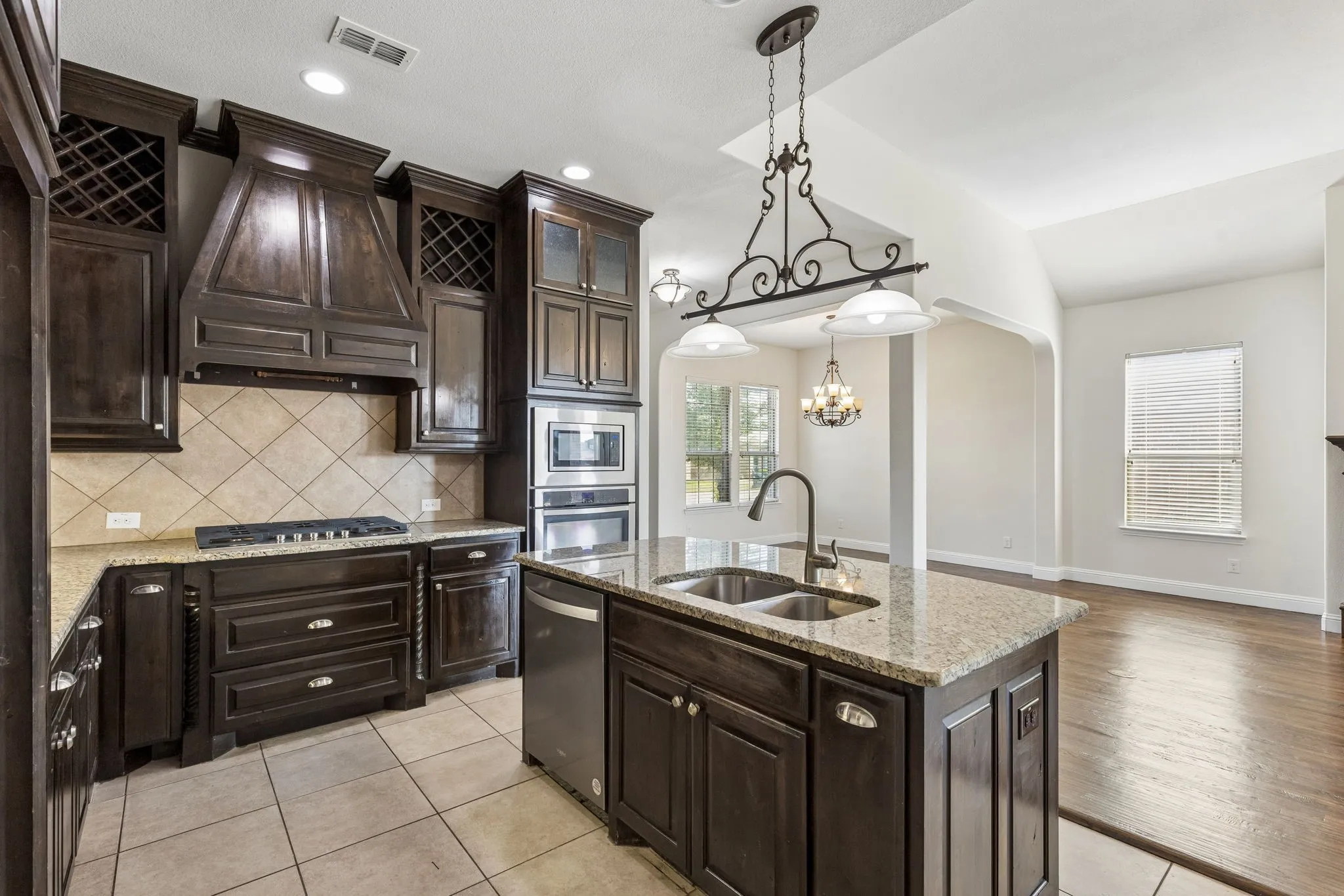 Kitchen featuring dark wood cabinetry, a built-in oven and microwave, a gas cooktop, an integrated dishwasher, and a center island with a double sink and pendant lighting