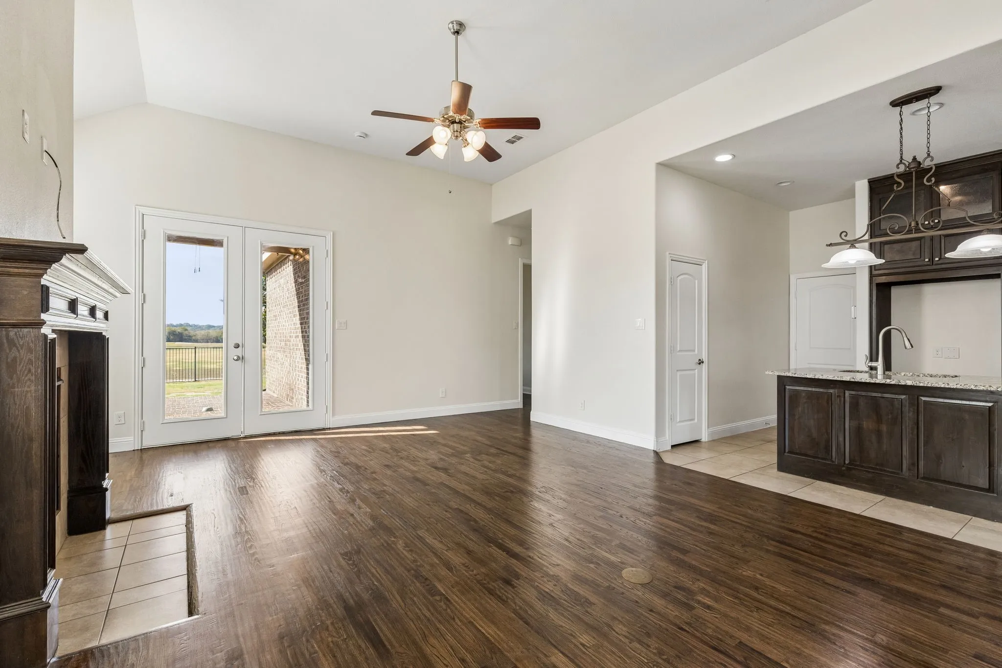 Vaulted ceilings with a ceiling fan, wood-finish flooring, French doors, a dark wood-finish fireplace, and an open-concept kitchen with granite countertops