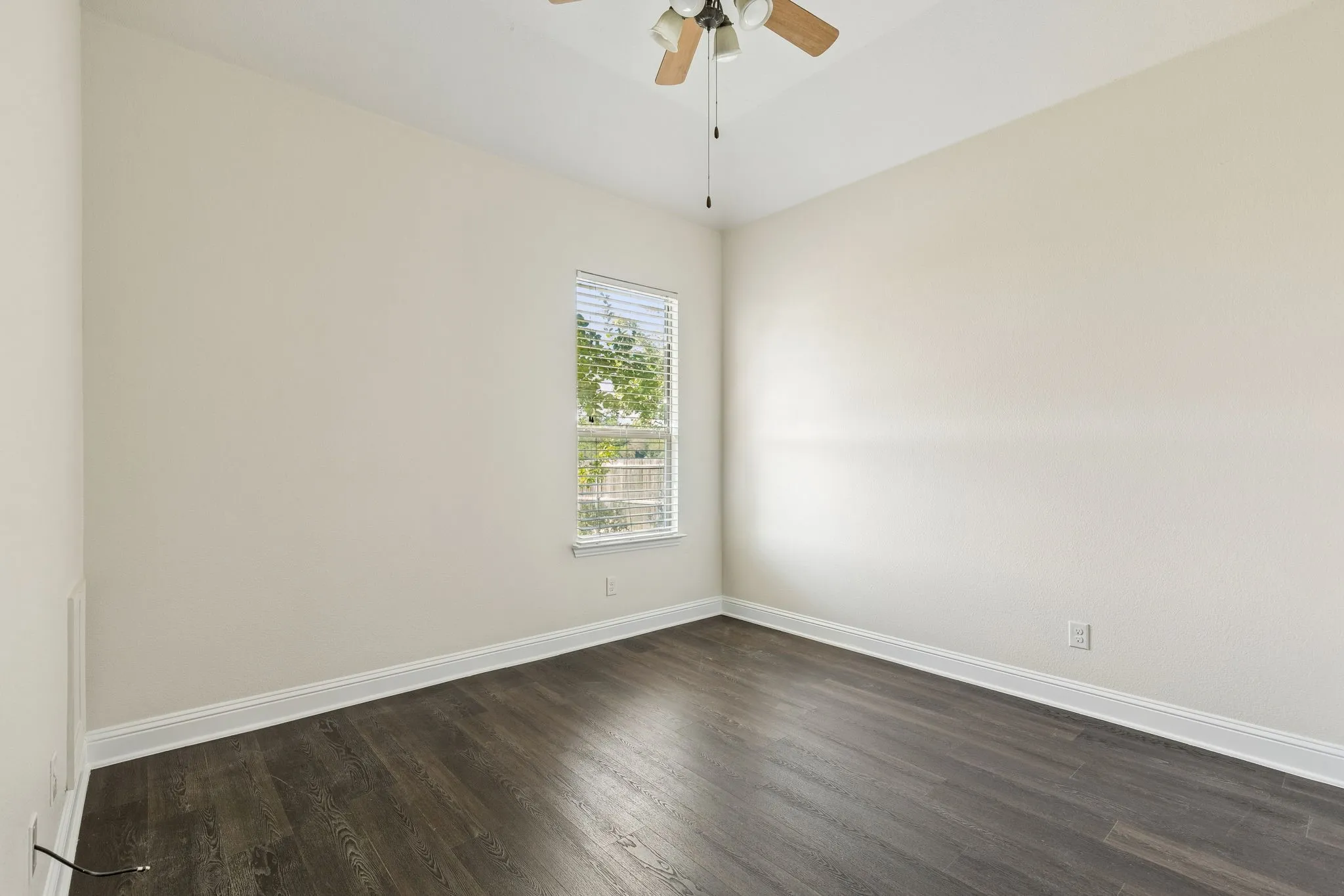 Wood-finish flooring with white trim, a single window, and a ceiling fan with integrated lighting