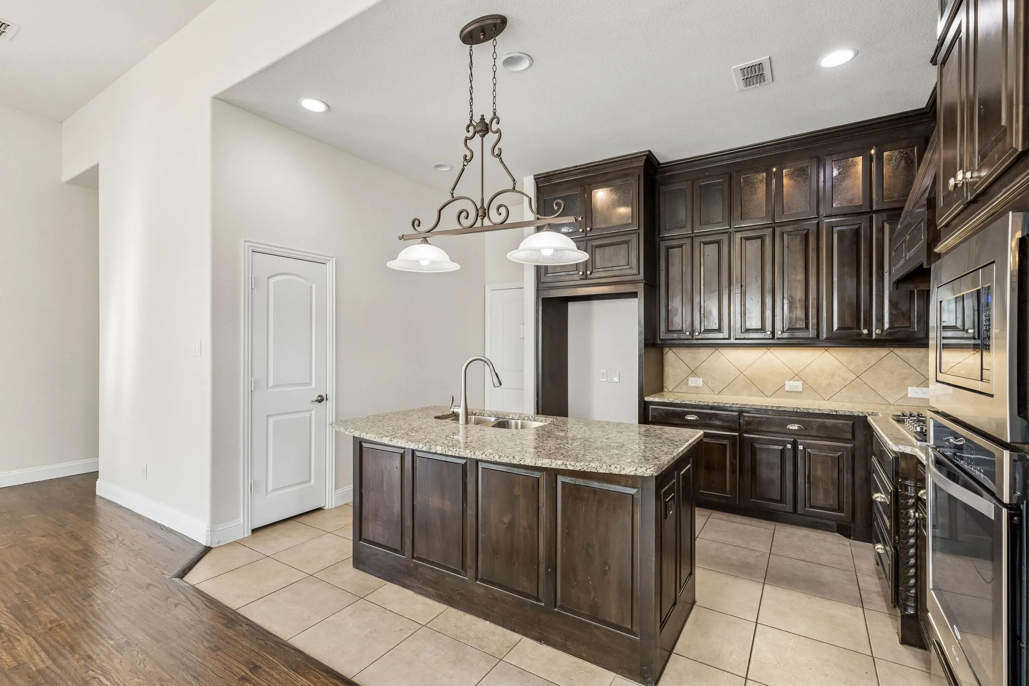 Kitchen featuring dark wood cabinetry, stainless steel appliances, a center island with sink, granite countertops, and tile flooring
