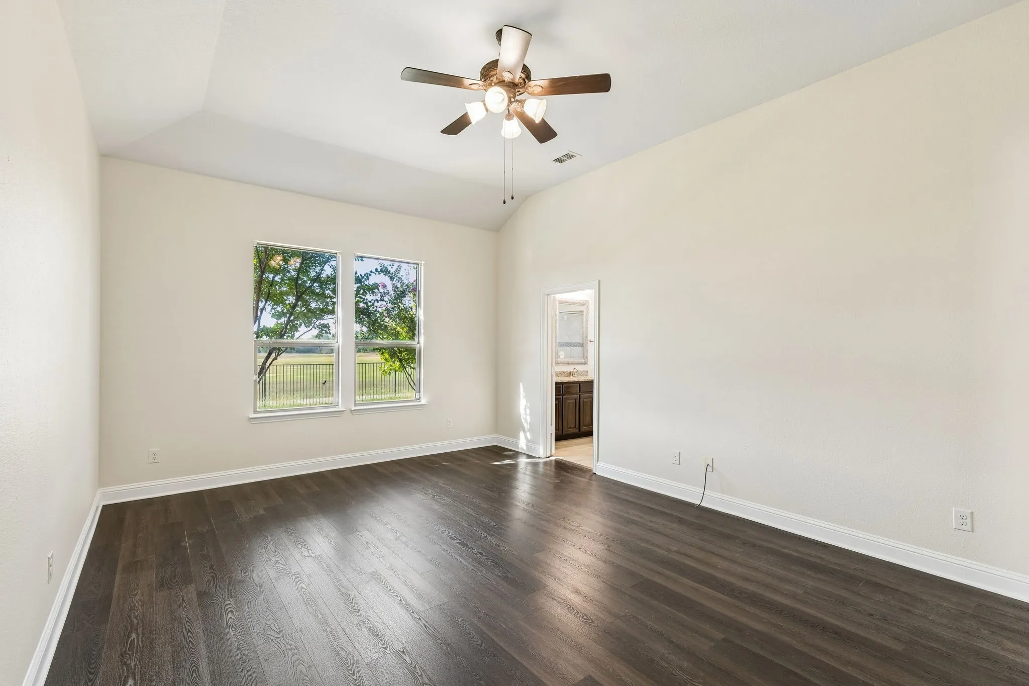 Vaulted ceiling with a ceiling fan, dual windows, wood-finish flooring, and white trim