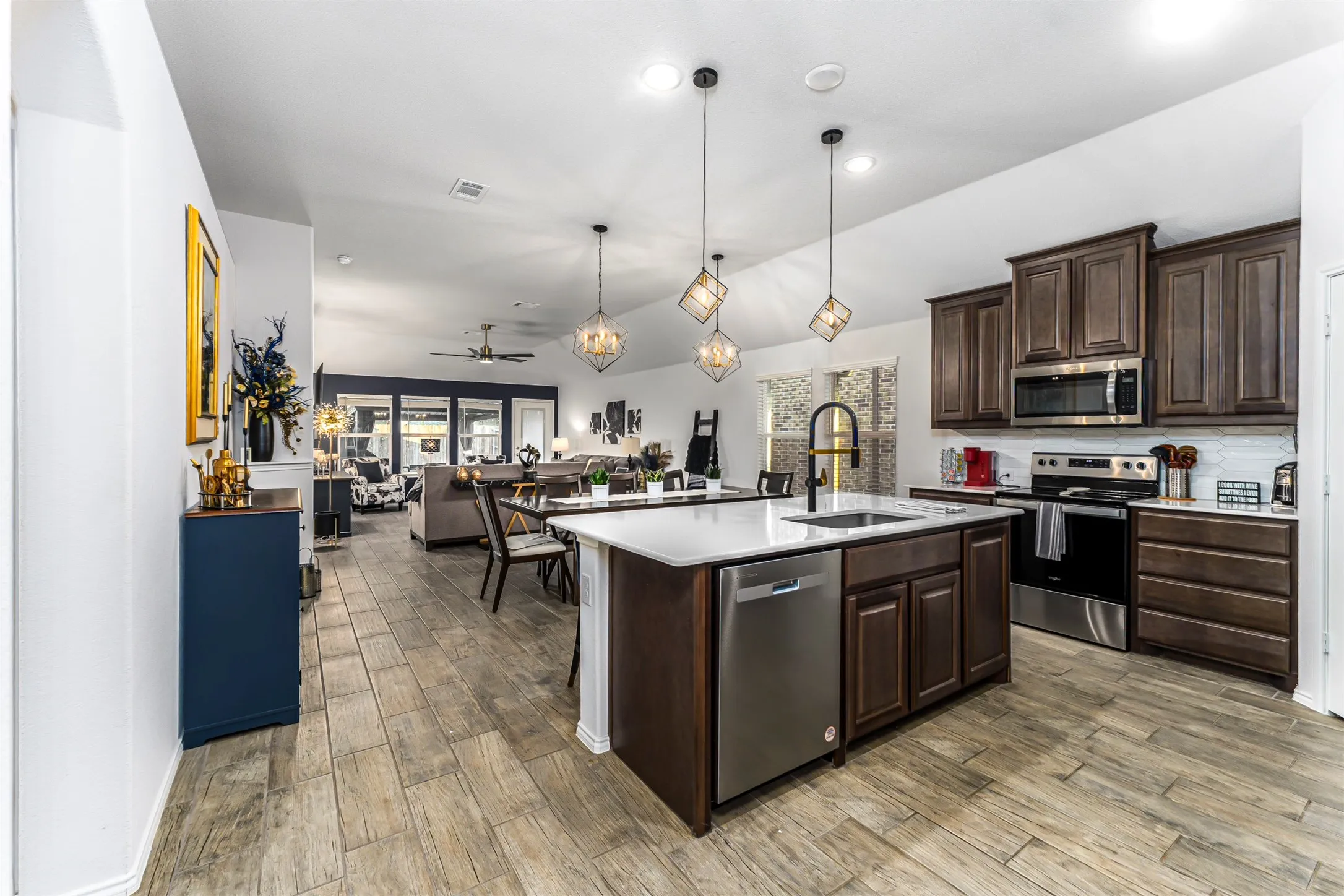 Open-concept kitchen featuring an island with a sink, stainless steel appliances, dark wood-finish cabinetry, and wood-finish tile flooring