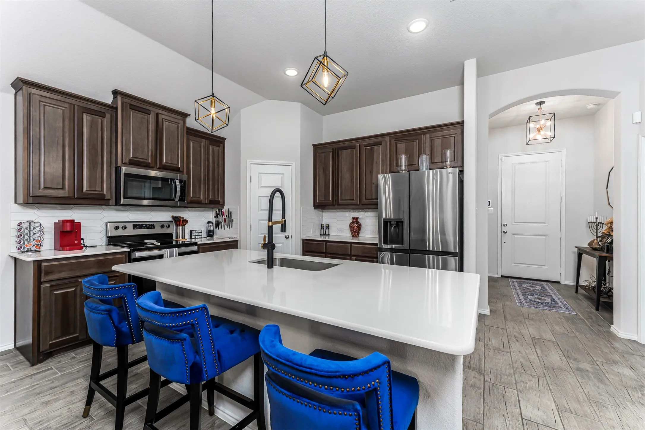 Kitchen featuring dark wood-finish cabinetry, white subway tile backsplash, stainless steel appliances, and a central island with a white countertop