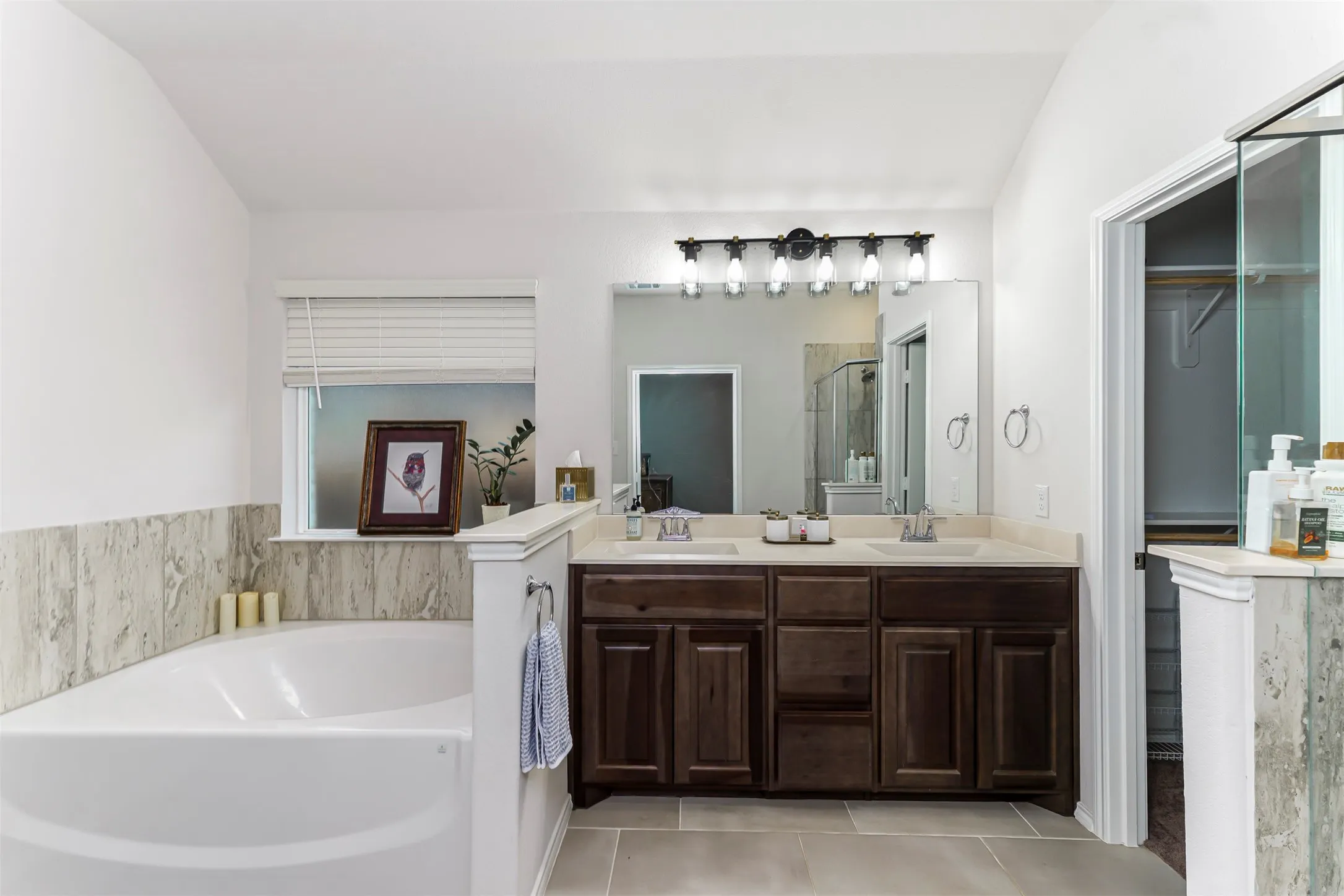 Dual sink vanity with wood-finish cabinetry, a framed mirror, and a multi-bulb light fixture
