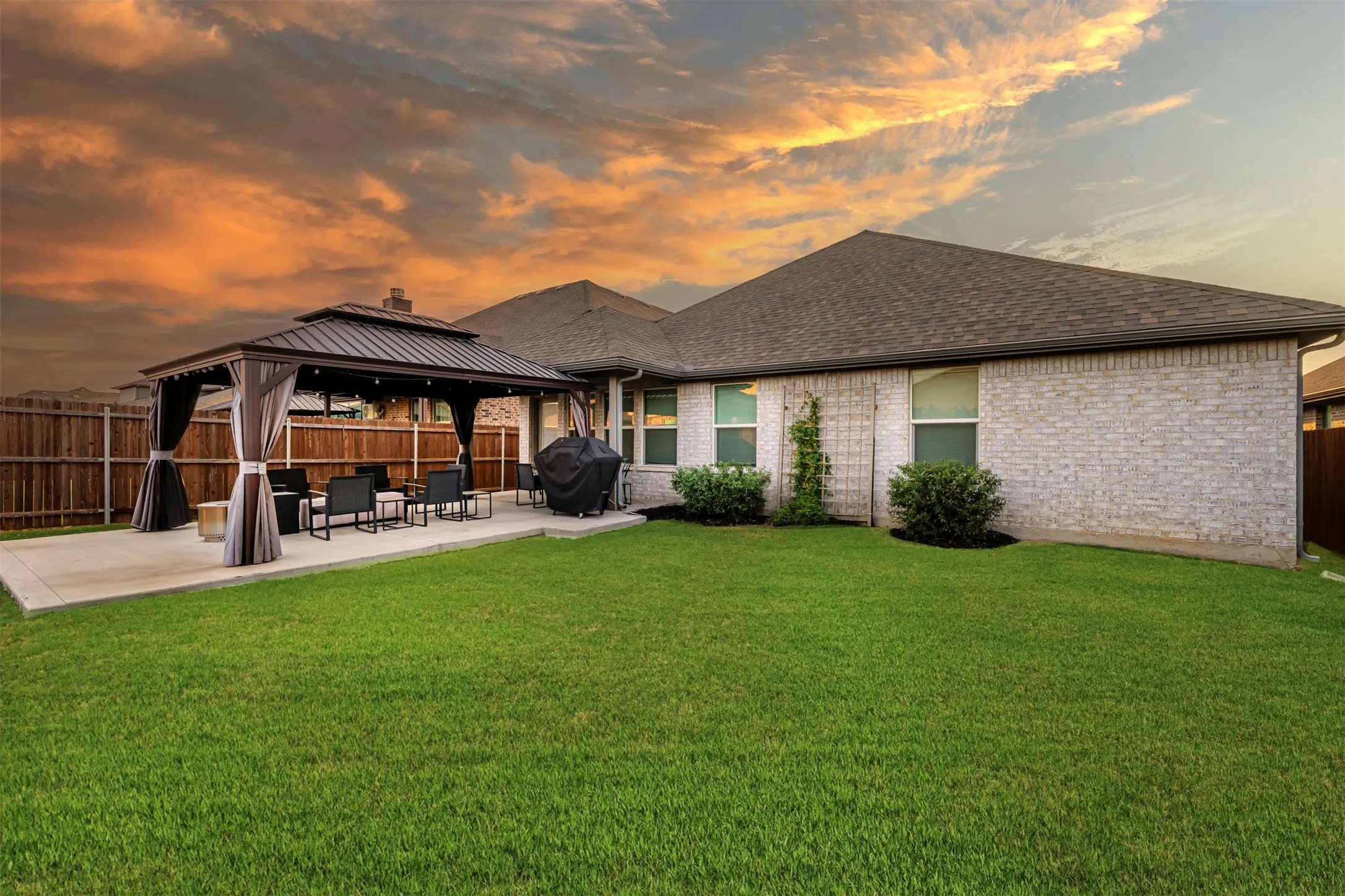 Expansive backyard featuring a lush lawn, concrete patio, and a built-in gazebo with a metal roof