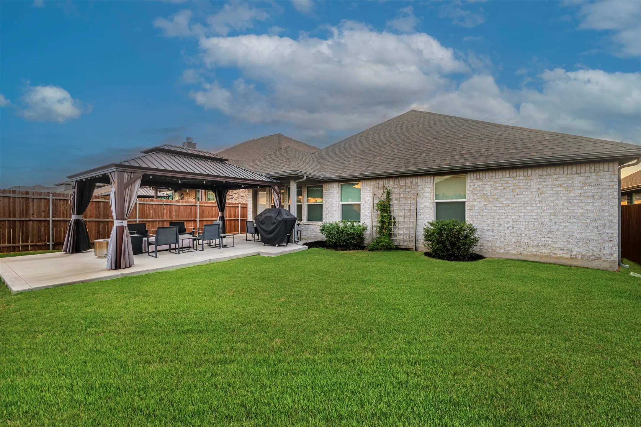 Expansive backyard featuring a manicured lawn, a large concrete patio, and a built-in gazebo