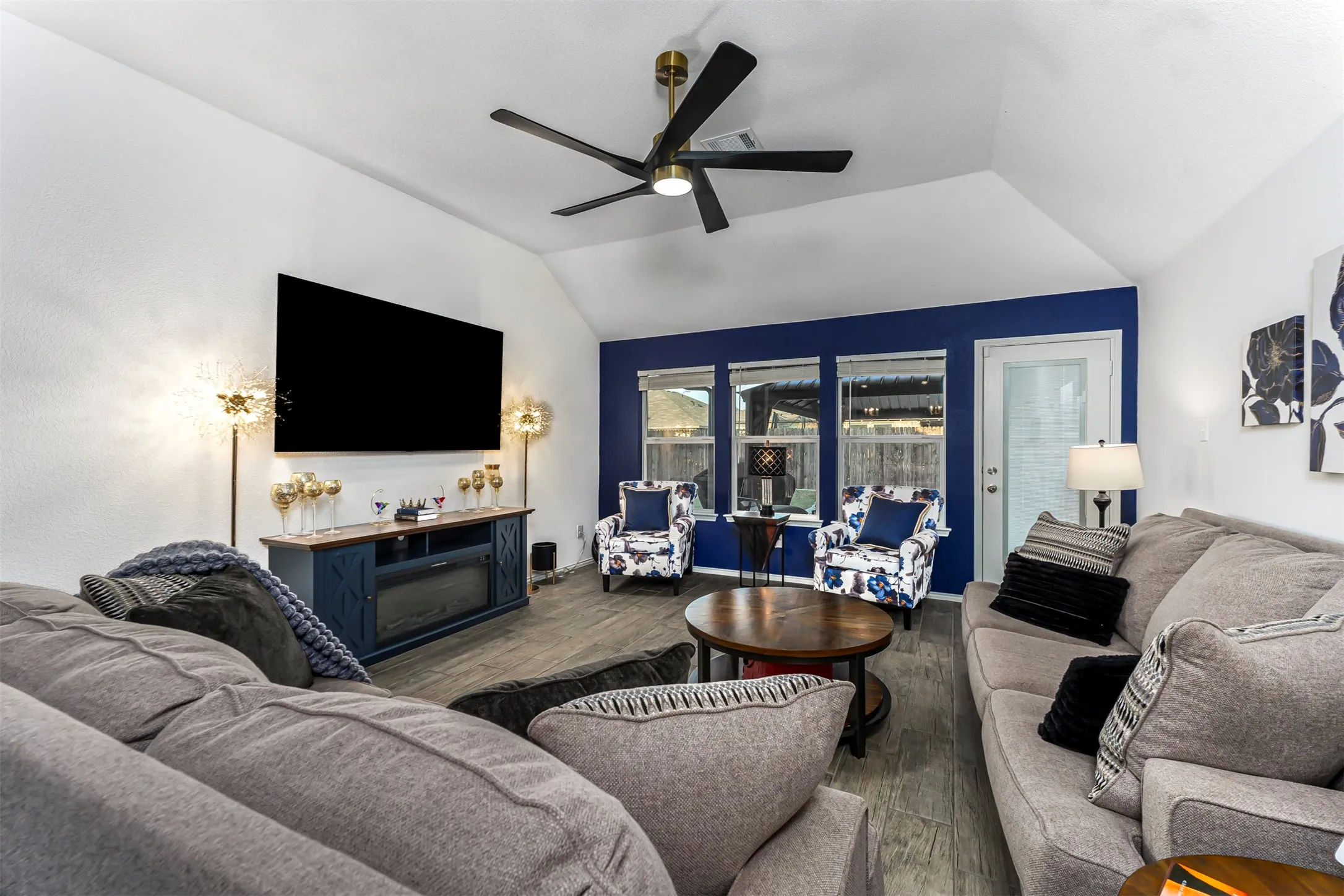 Vaulted ceiling with a black ceiling fan, wood-finish flooring, and a built-in media console with an electric fireplace