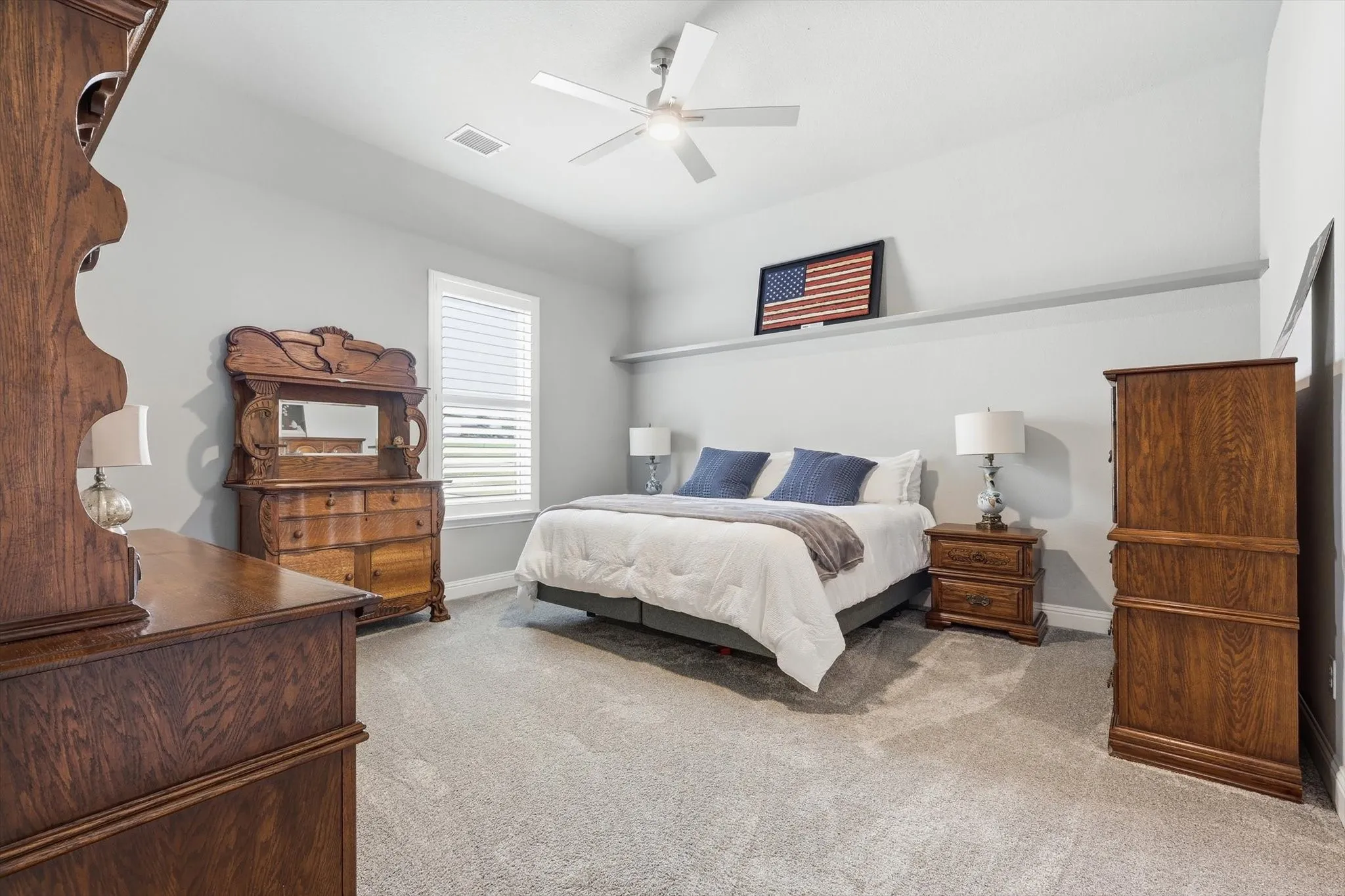 Carpeted flooring throughout, overhead ceiling fan, white window blinds, and a built-in wall shelf