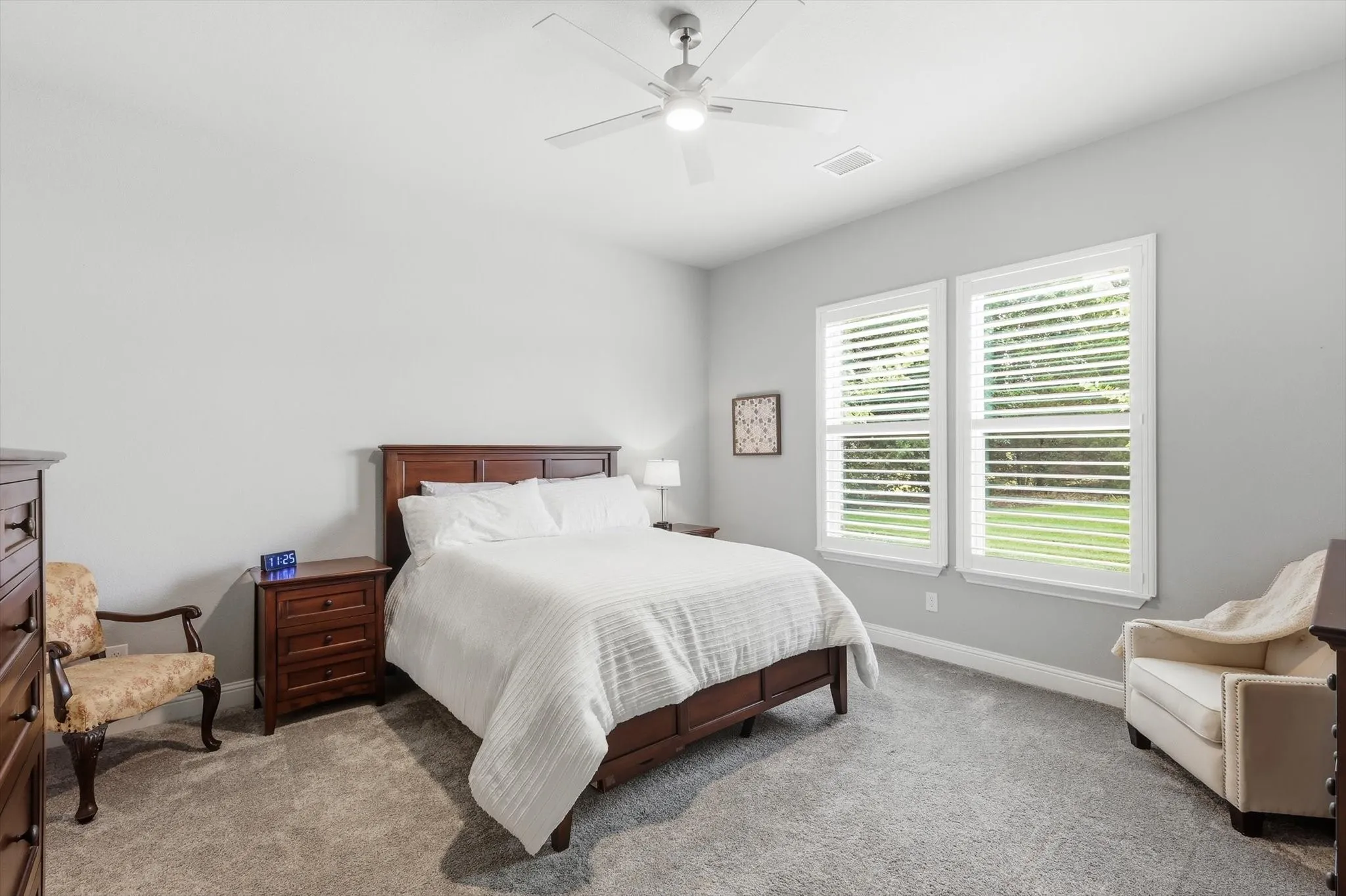 Carpeted bedroom featuring two windows with plantation shutters, a ceiling fan, and painted walls