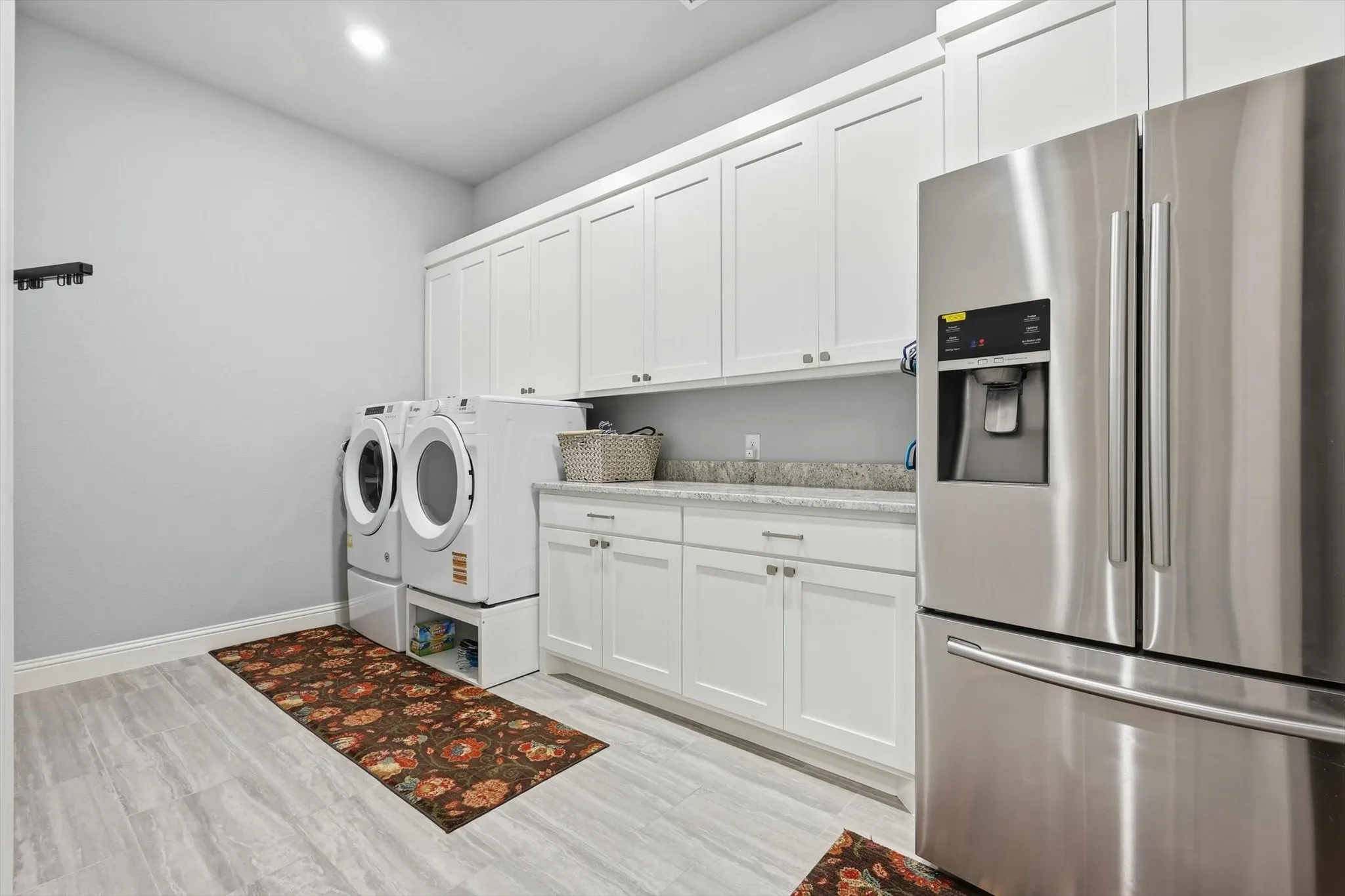 White shaker-style cabinetry with ample storage, integrated stainless steel refrigerator, light-toned wood-finish flooring, and a durable countertop