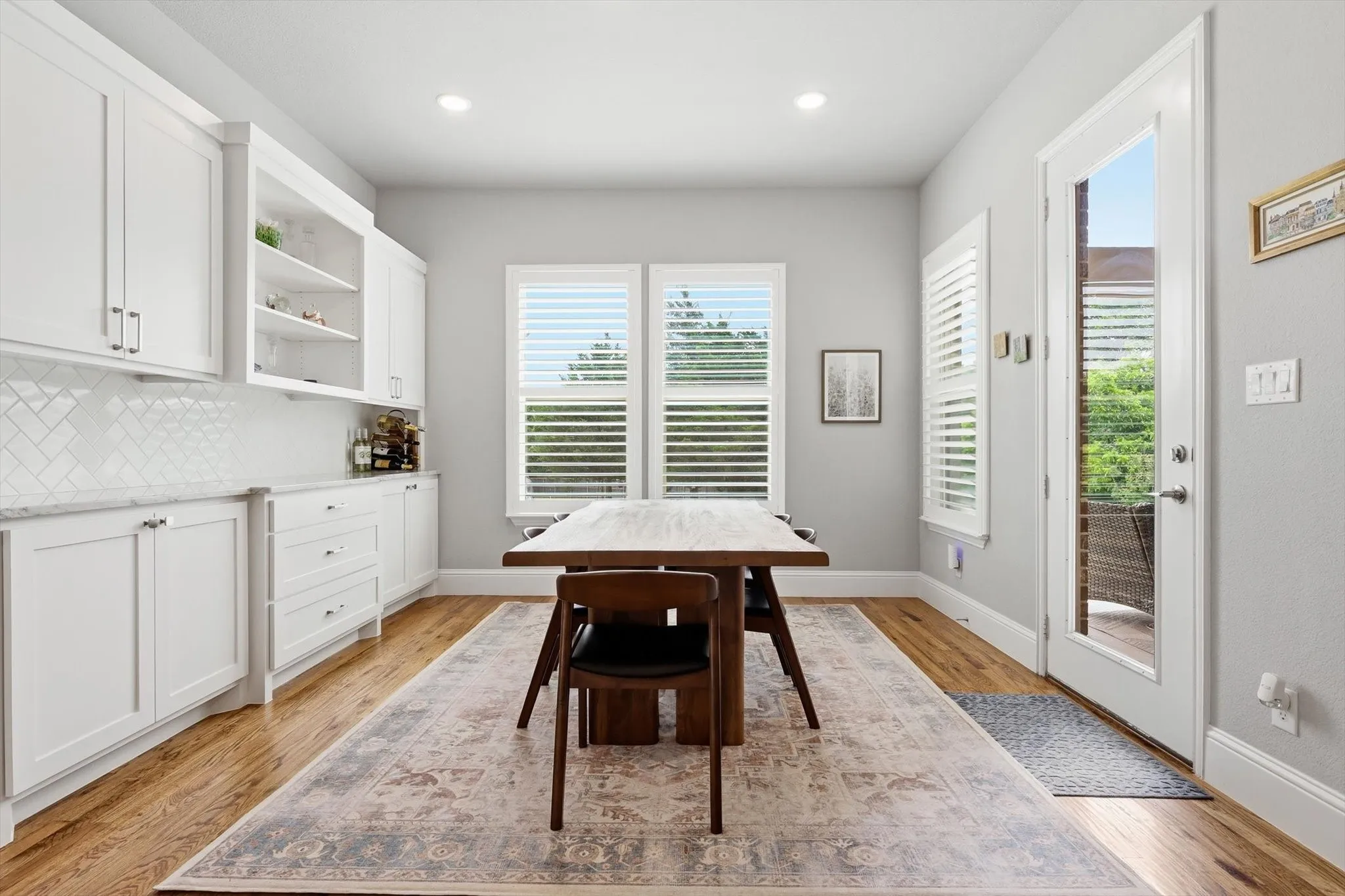 White shaker cabinetry with open shelving, herringbone tile backsplash, light wood-finish flooring, and a glass-paneled door
