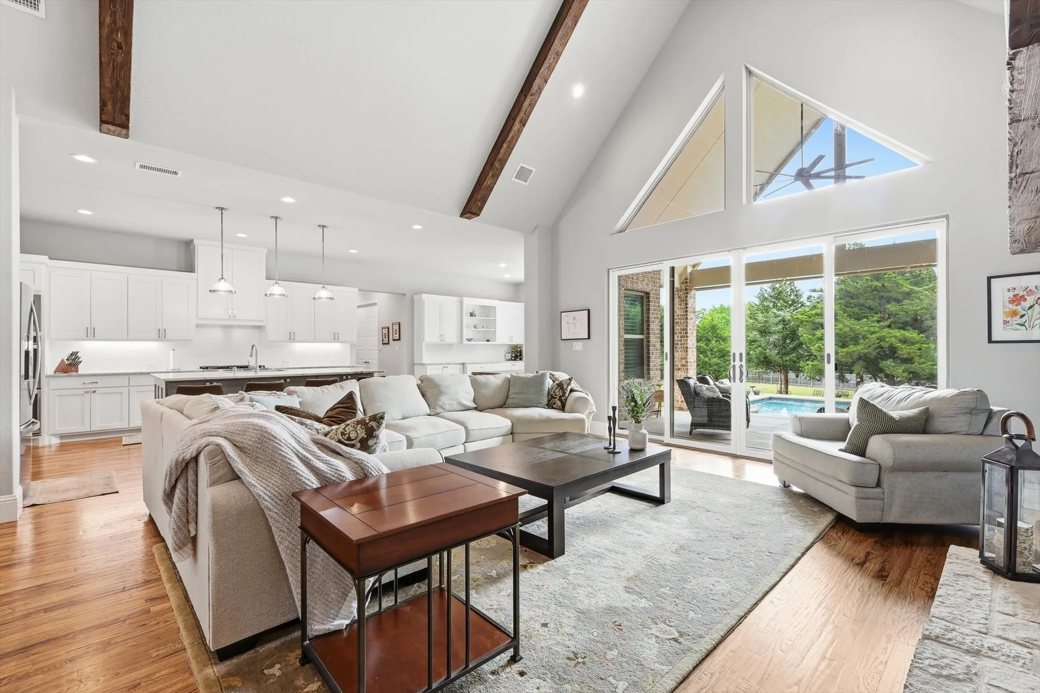 Vaulted ceiling with exposed wood beams, wood-finish flooring, white cabinetry with under-cabinet lighting, large sliding glass doors, and triangular transom windows