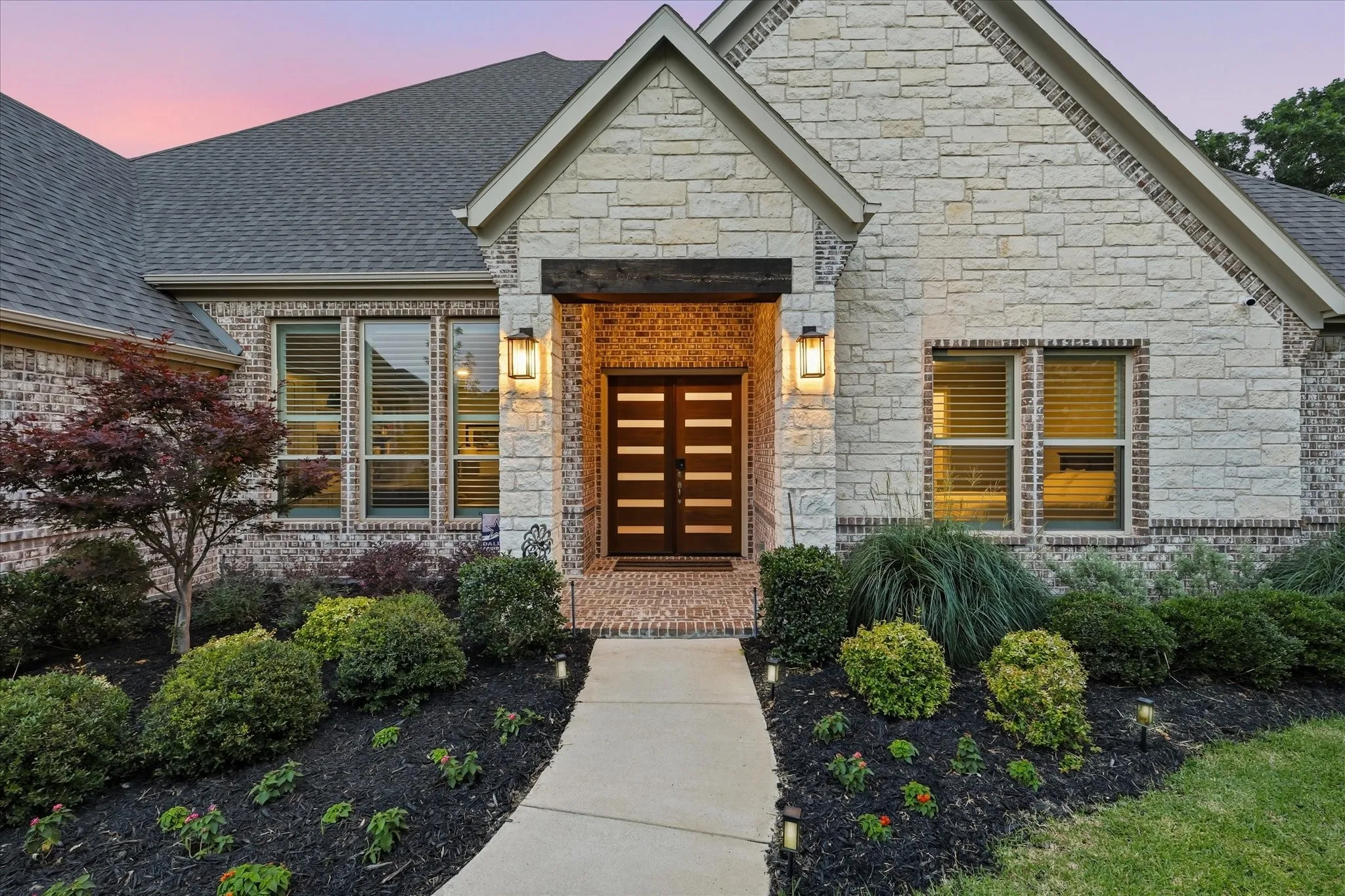 Stone and brick exterior with a multi-pane entry door, complemented by dual outdoor sconces and a paved walkway