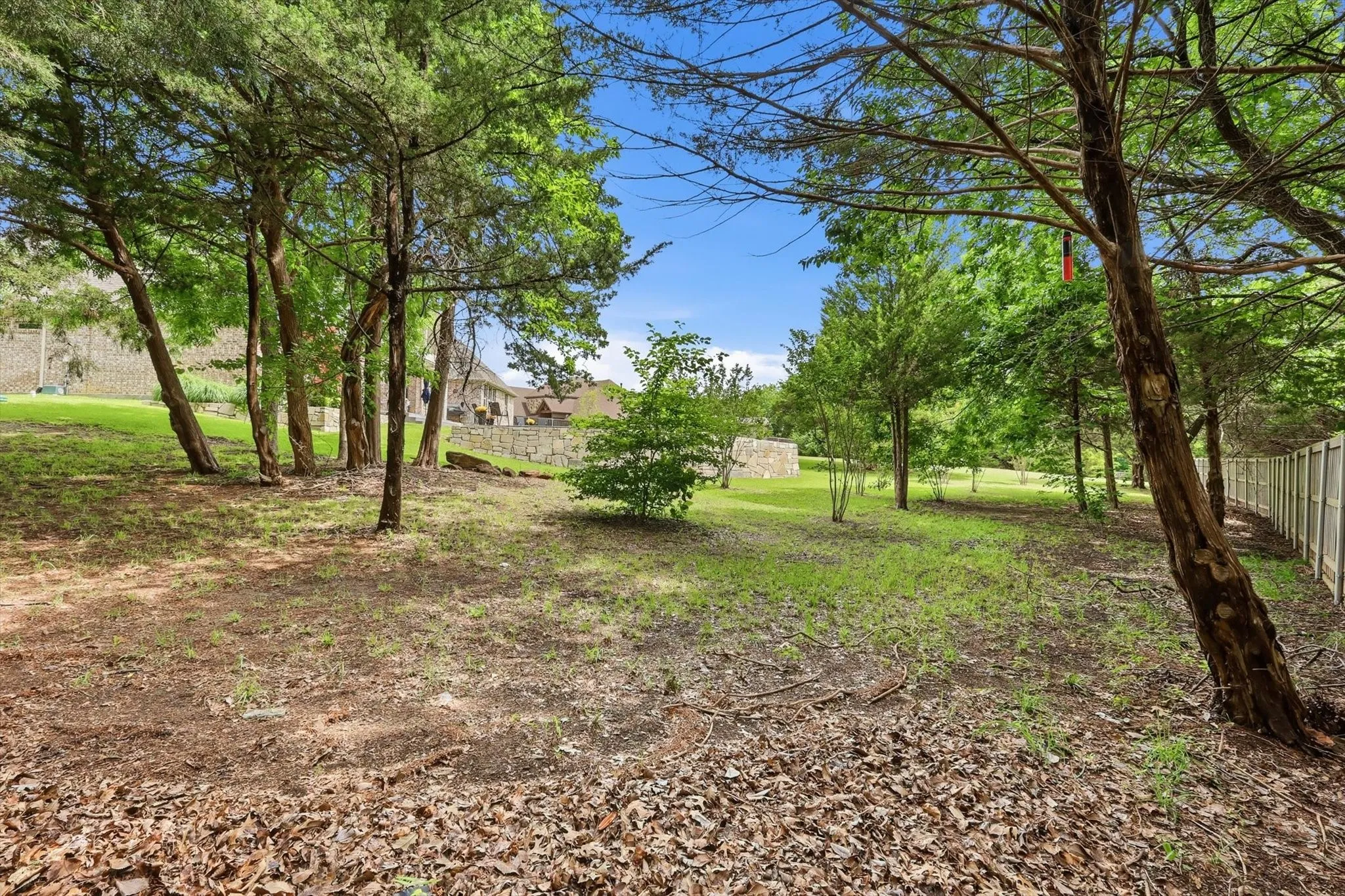 Expansive rear yard featuring mature trees, a privacy fence, and a stone retaining wall