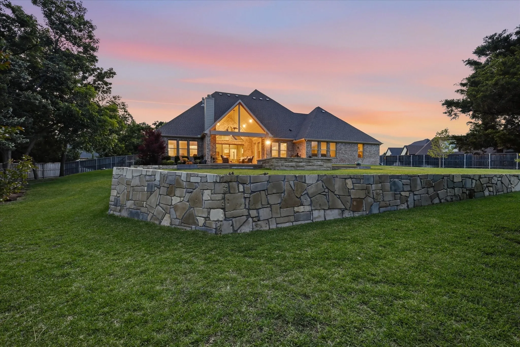 Stone retaining wall and expansive green lawn, featuring a brick and stone exterior, gabled roofline, and abundant windows