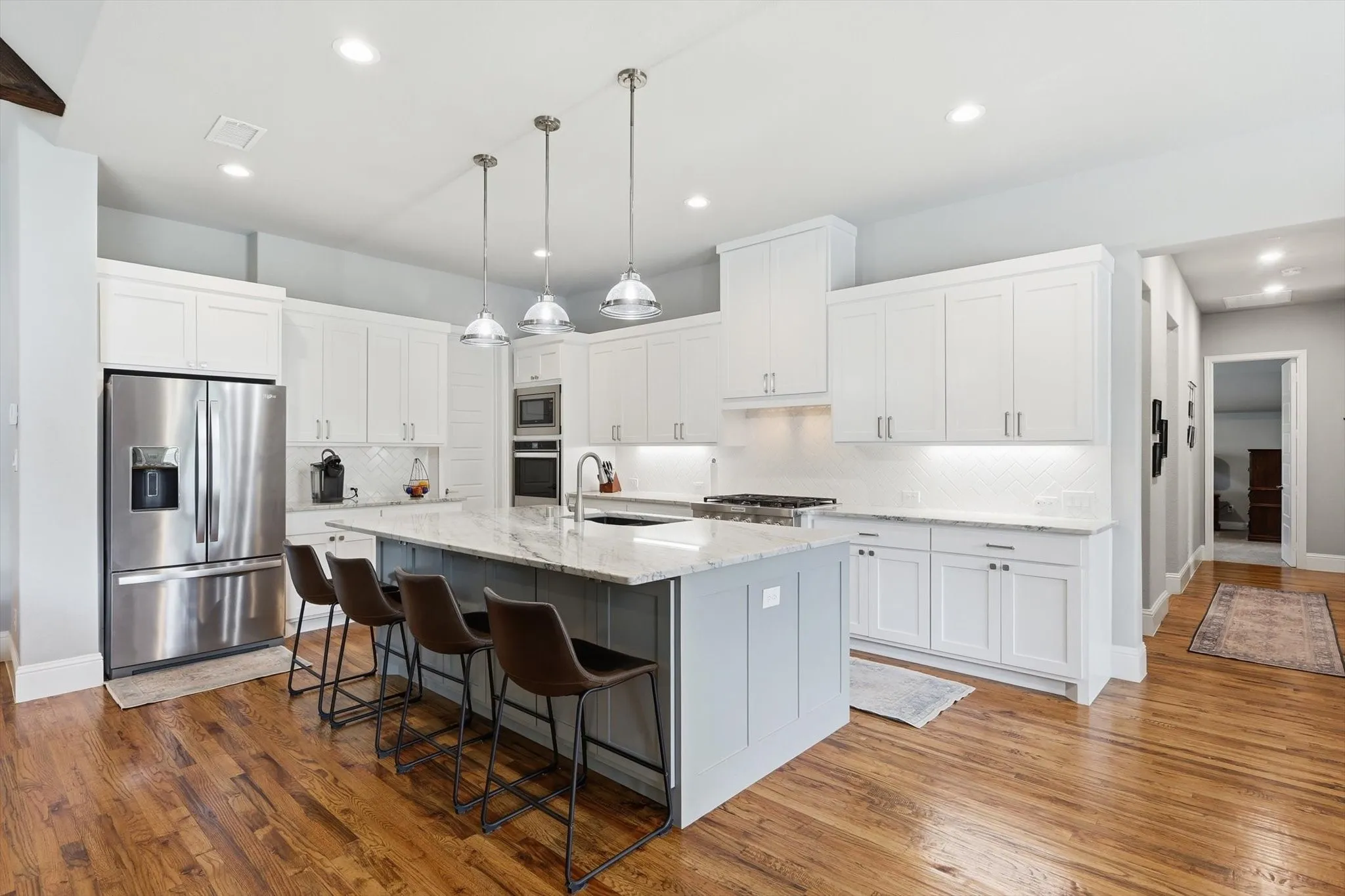 Kitchen featuring wood-finish flooring, white cabinetry, stainless steel appliances, a center island with pendant lighting, and light-toned countertops