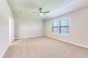 Spacious room with plush carpeting, neutral wall finishes, a ceiling fan, and two windows with blinds