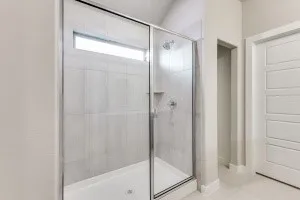 Glass-enclosed shower with a transom window, tiled walls, a built-in niche, and a shower head with separate controls