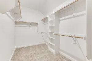 Walk-in closet featuring built-in shelving, hanging rods, and light-toned carpet flooring