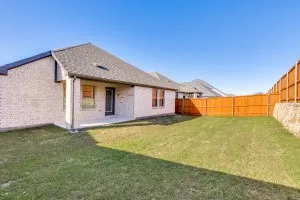 Expansive backyard featuring a manicured lawn, wood privacy fence, and a stone retaining wall