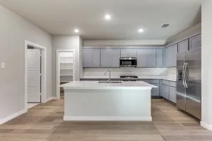 Kitchen featuring light gray cabinetry, stainless steel appliances, a center island with sink, white countertops, and wood-finish flooring