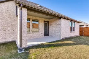 Covered concrete patio with a brick exterior, framed by a wooden fence