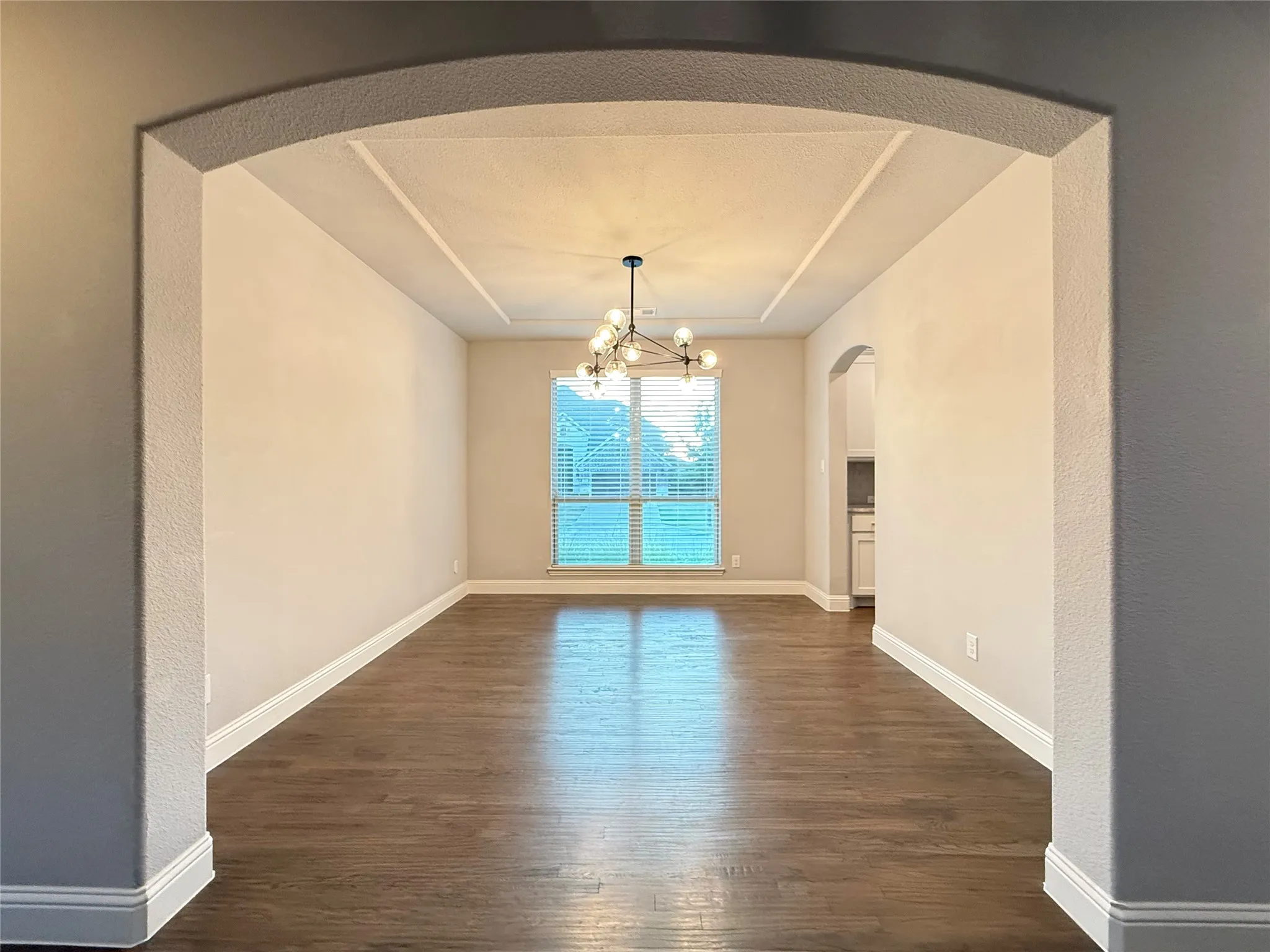 Archway entry to a room featuring wood-finish flooring, a tray ceiling, and a modern chandelier