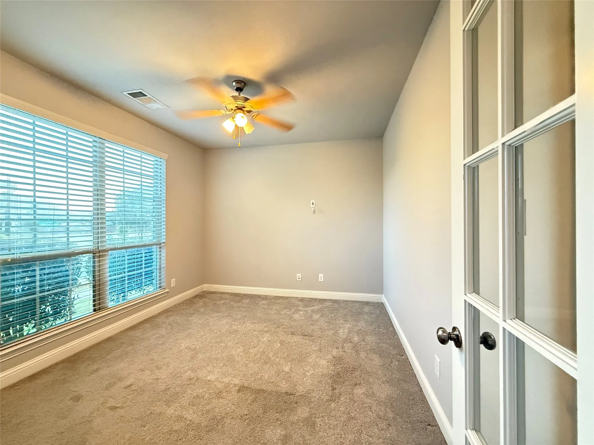 Recessed window with blinds, ceiling fan with integrated lighting, carpeted flooring, and French doors with dark hardware