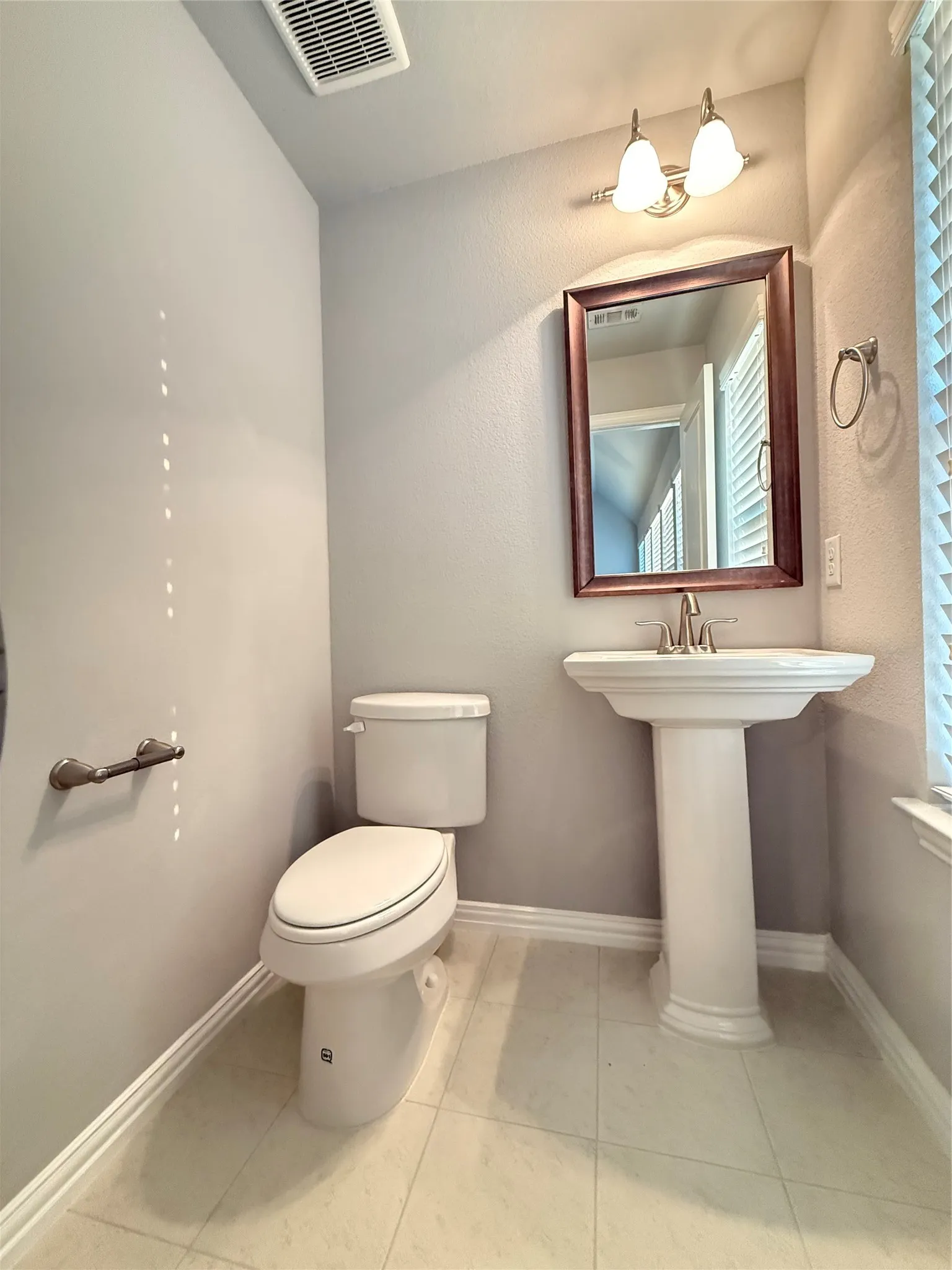Pedestal sink with polished chrome faucet, framed mirror, and dual-bulb vanity light