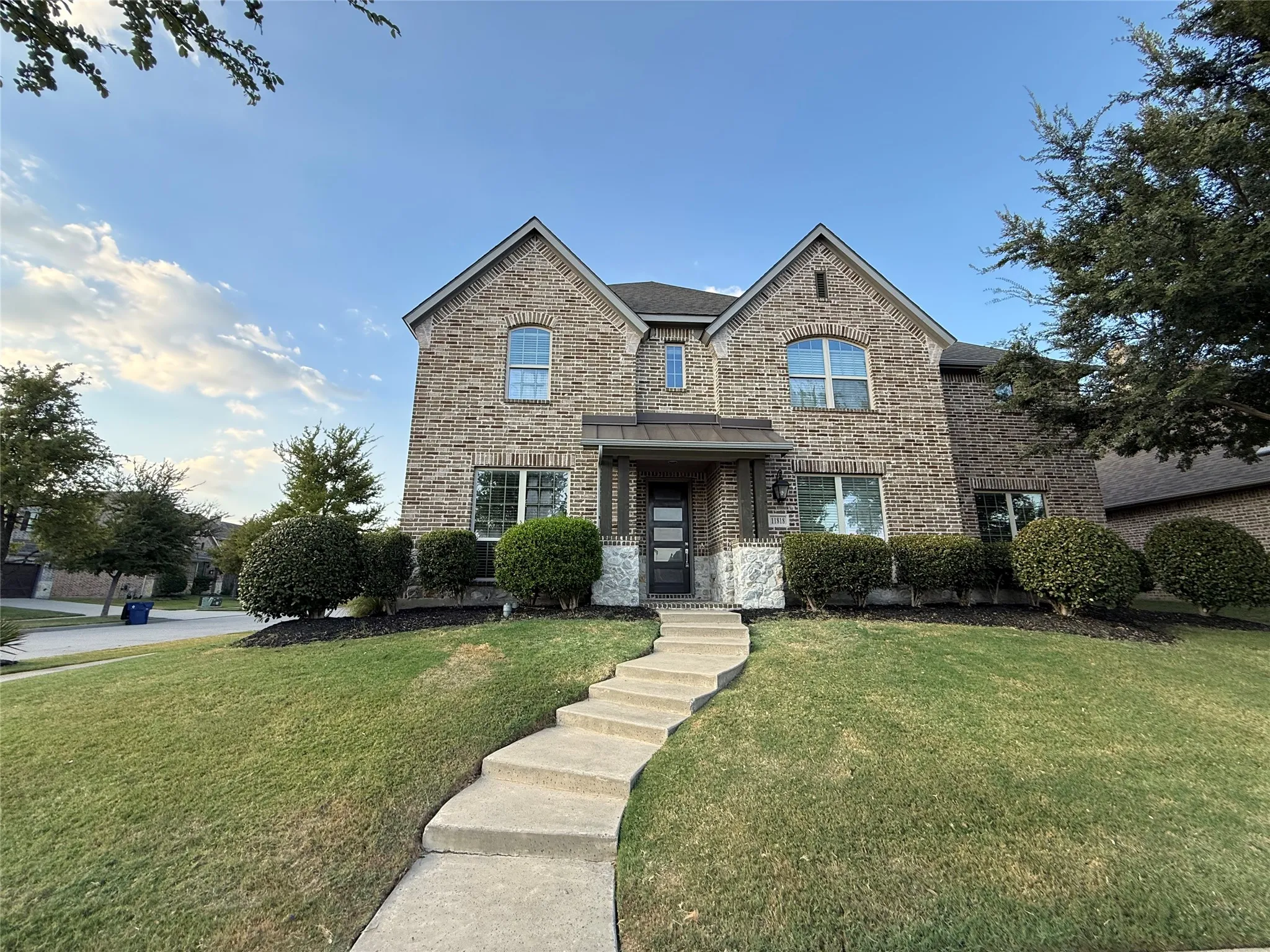 Brick facade with stone accents, a landscaped front yard, a meandering concrete pathway, and mature shrubbery